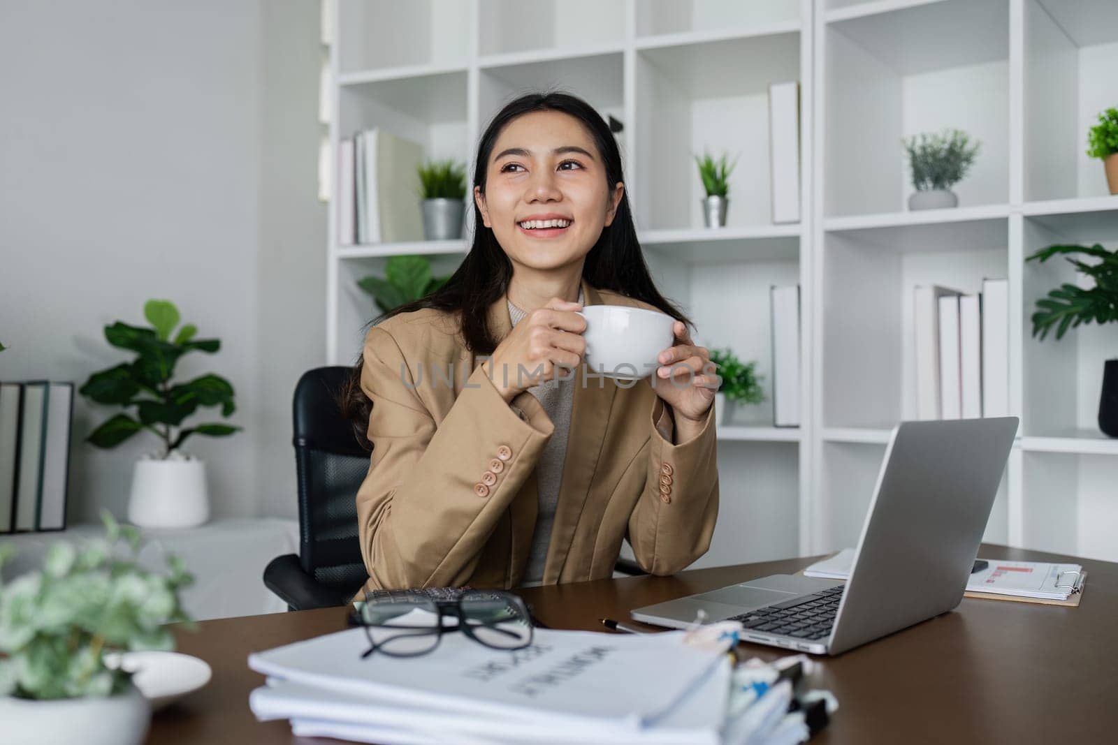 smiling businesswoman drinking coffee and working on laptop in green modern office. Nice Environment Office. Eco-Friendly Concept.