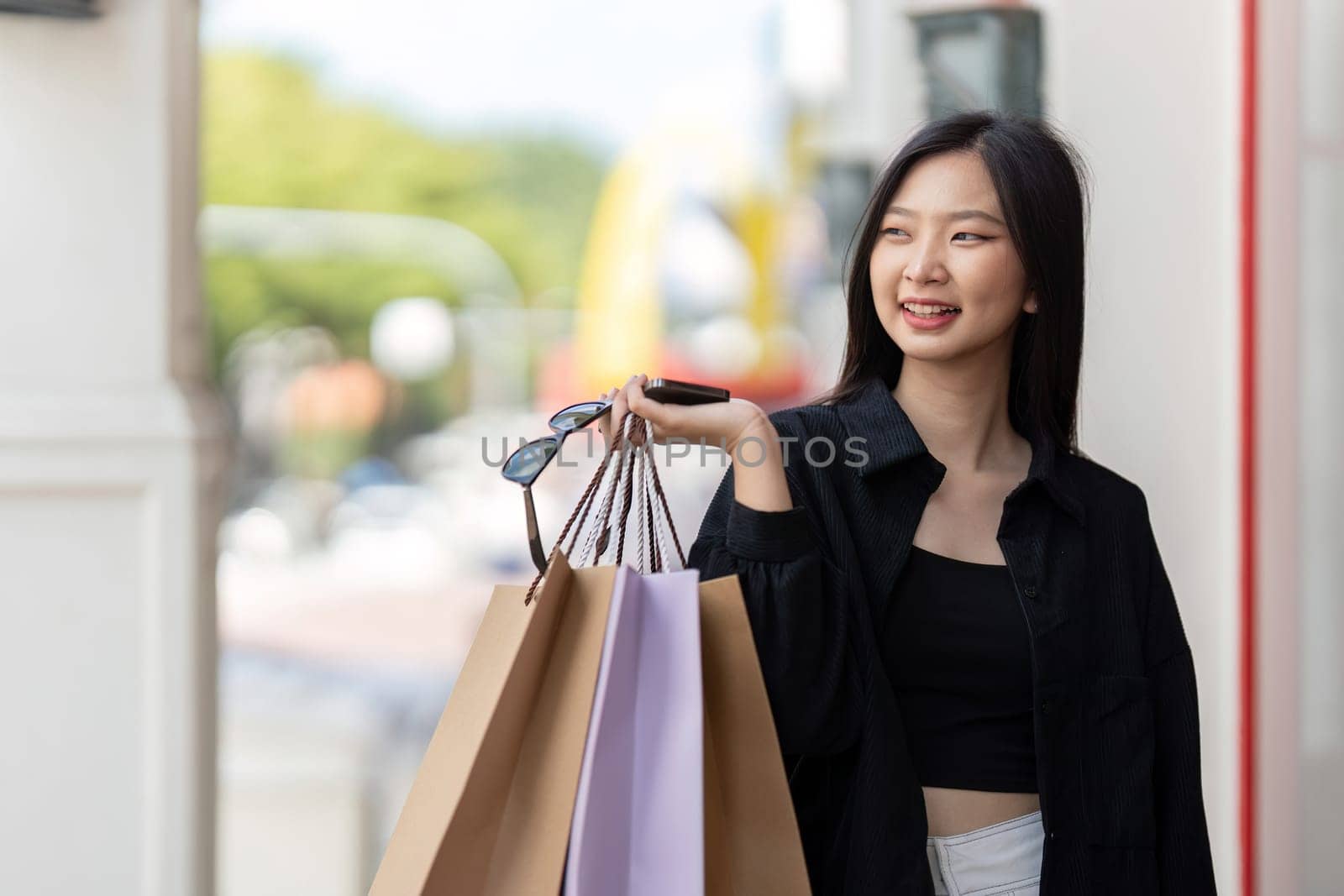 Cheerful Beautiful Asian woman holding shopping bags in shopping in the city on holiday Black Friday.