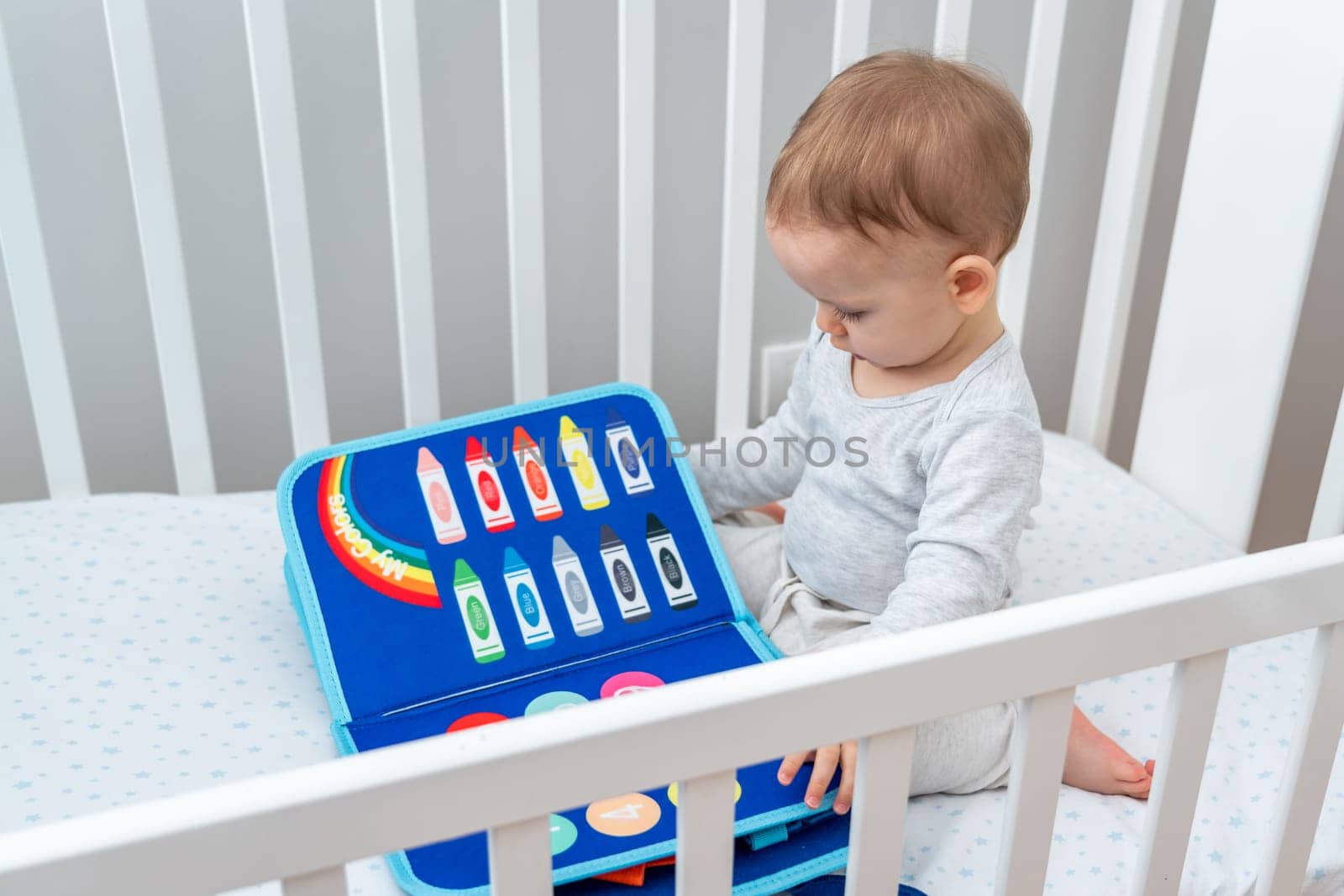 Baby playing with montessori busy book sitting in crib. Educational books and quiet books concept. Montessori busy board by Mariakray