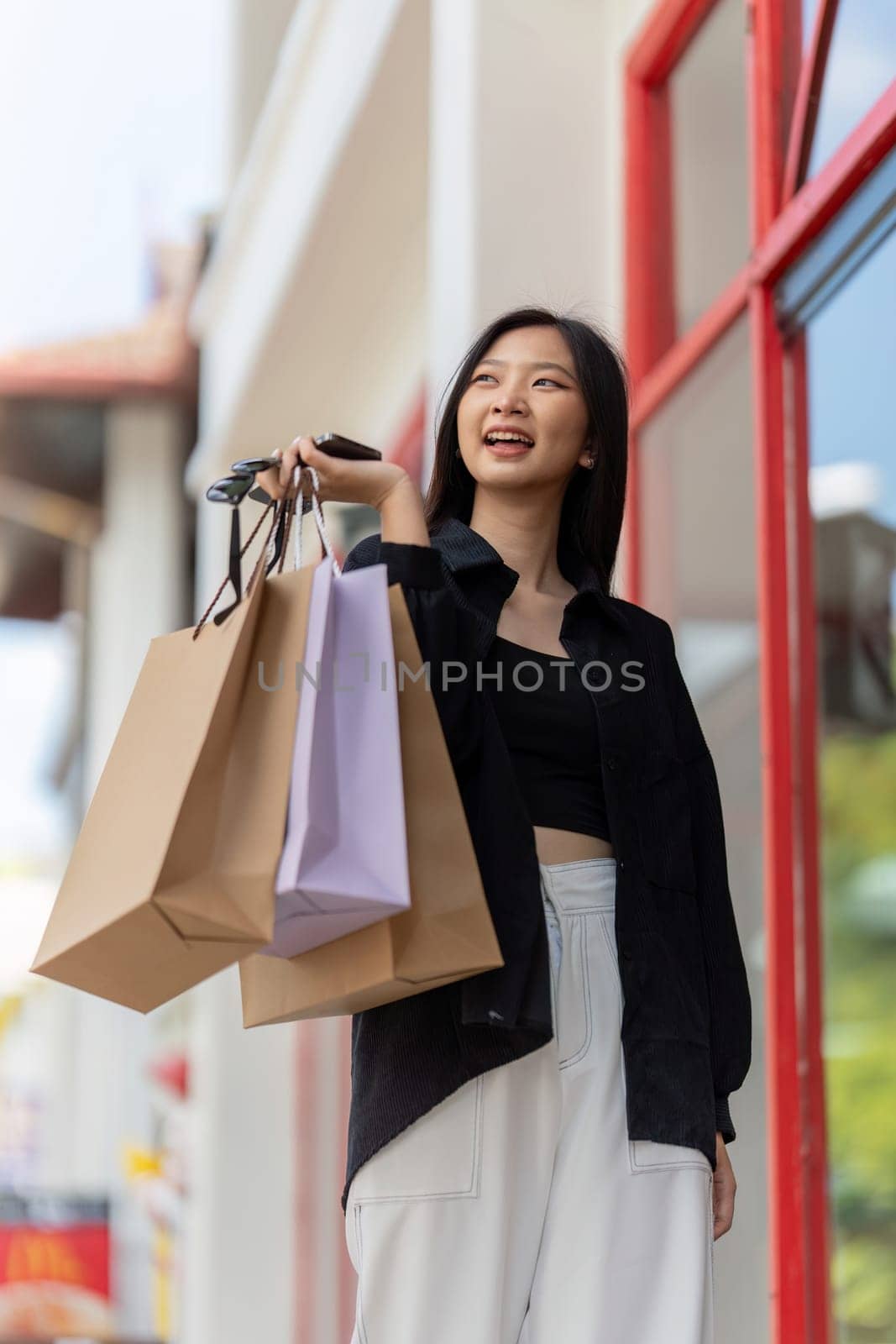 Cheerful Beautiful Asian woman holding shopping bags in shopping in the city on holiday Black Friday by nateemee