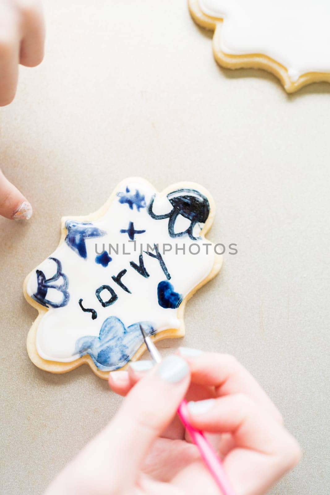 A heartwarming scene of a little girl carefully writing 'Sorry' on sugar cookies with food coloring, the cookies beautifully flooded with white royal icing.