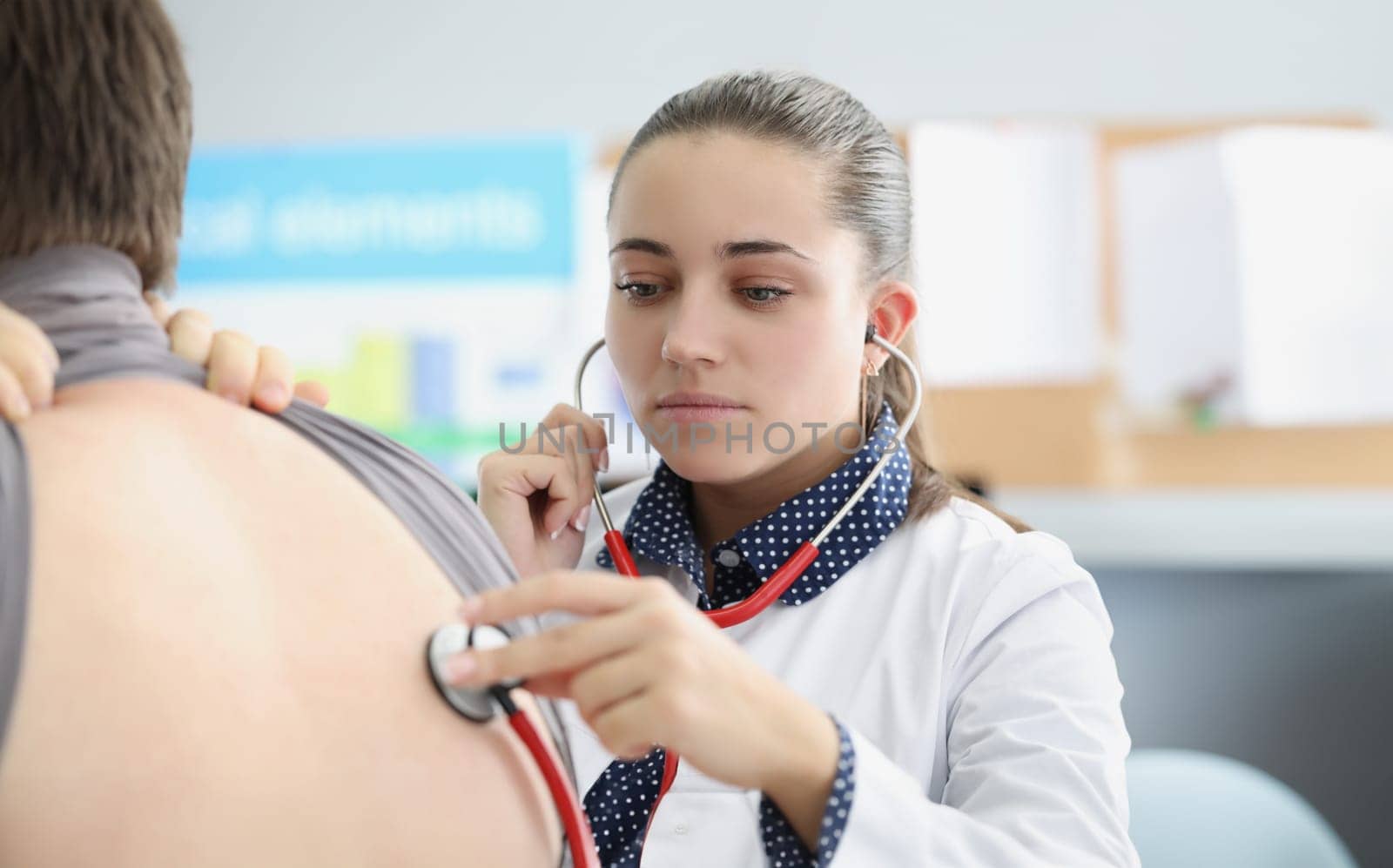 Woman pulmonologist listening to lungs of patient with stethoscope in clinic by kuprevich