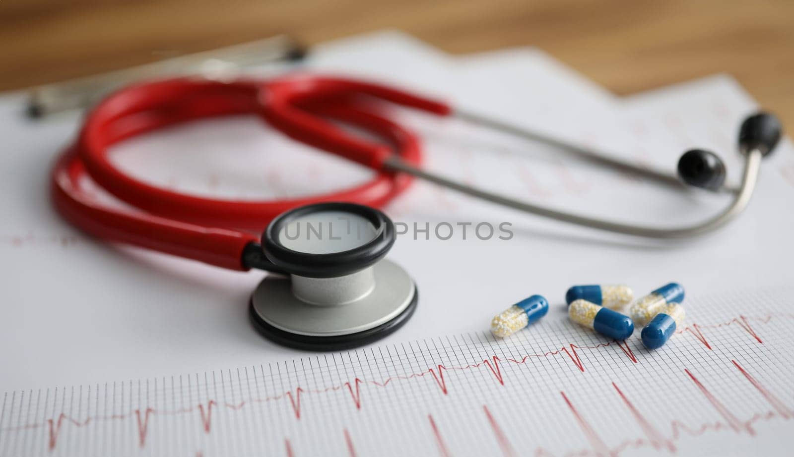 Medical capsules and red stethoscope lying on electrocardiogram closeup. Diagnostics and treatment of rhythm disturbances concept