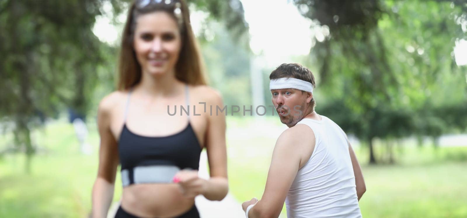 Fat man looking at young woman athlete jogging in park by kuprevich