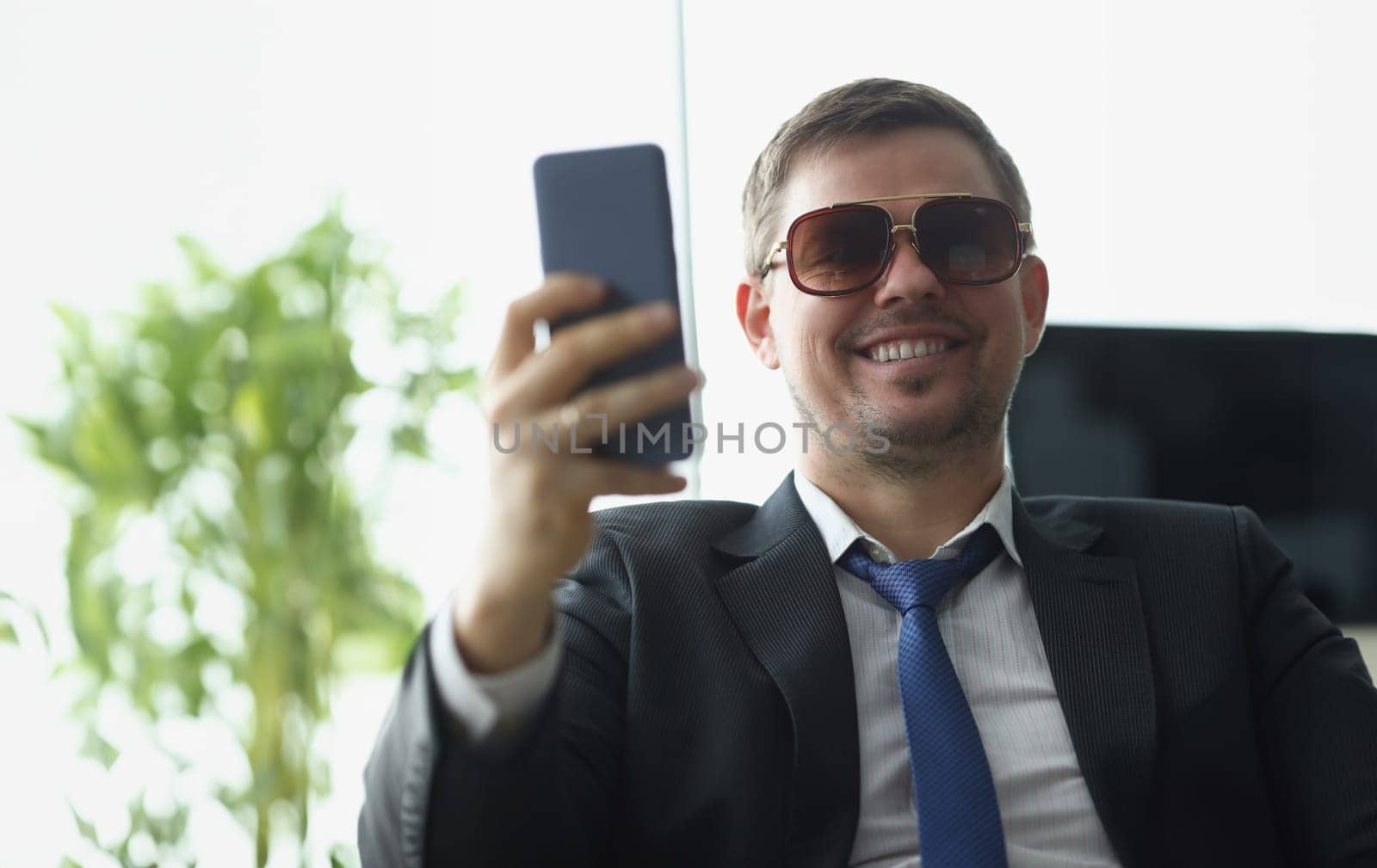 Businessman in sunglasses in suit looking at screen of mobile phone. Remote business concept