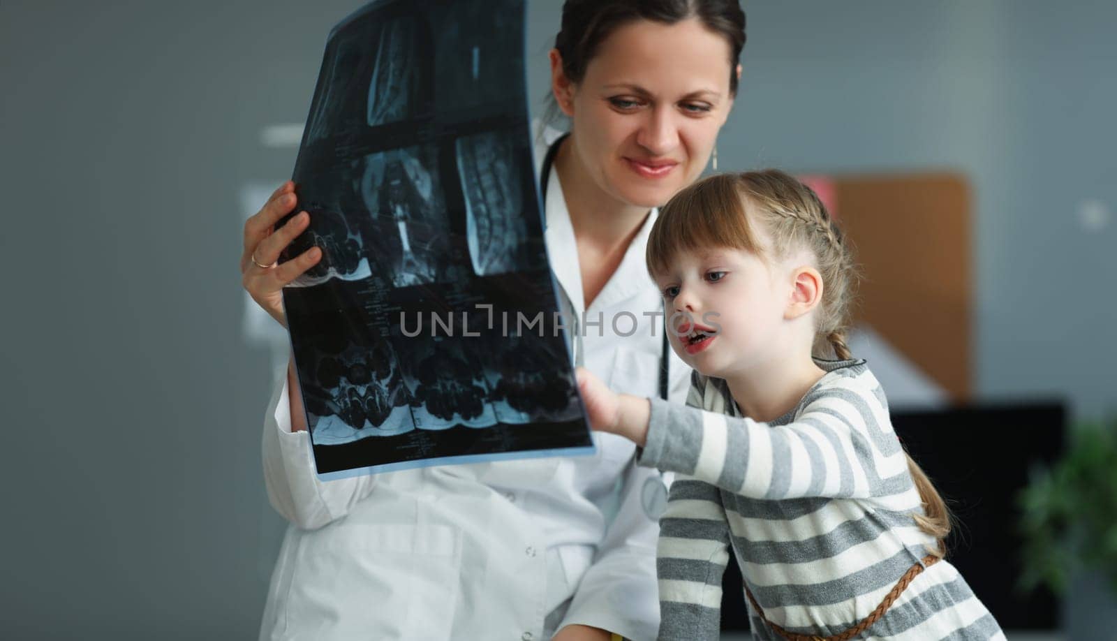 Woman doctor showing little girl xray in clinic by kuprevich