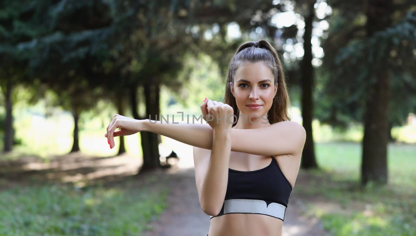 Young woman athlete stretches her hands before sports jog in park by kuprevich
