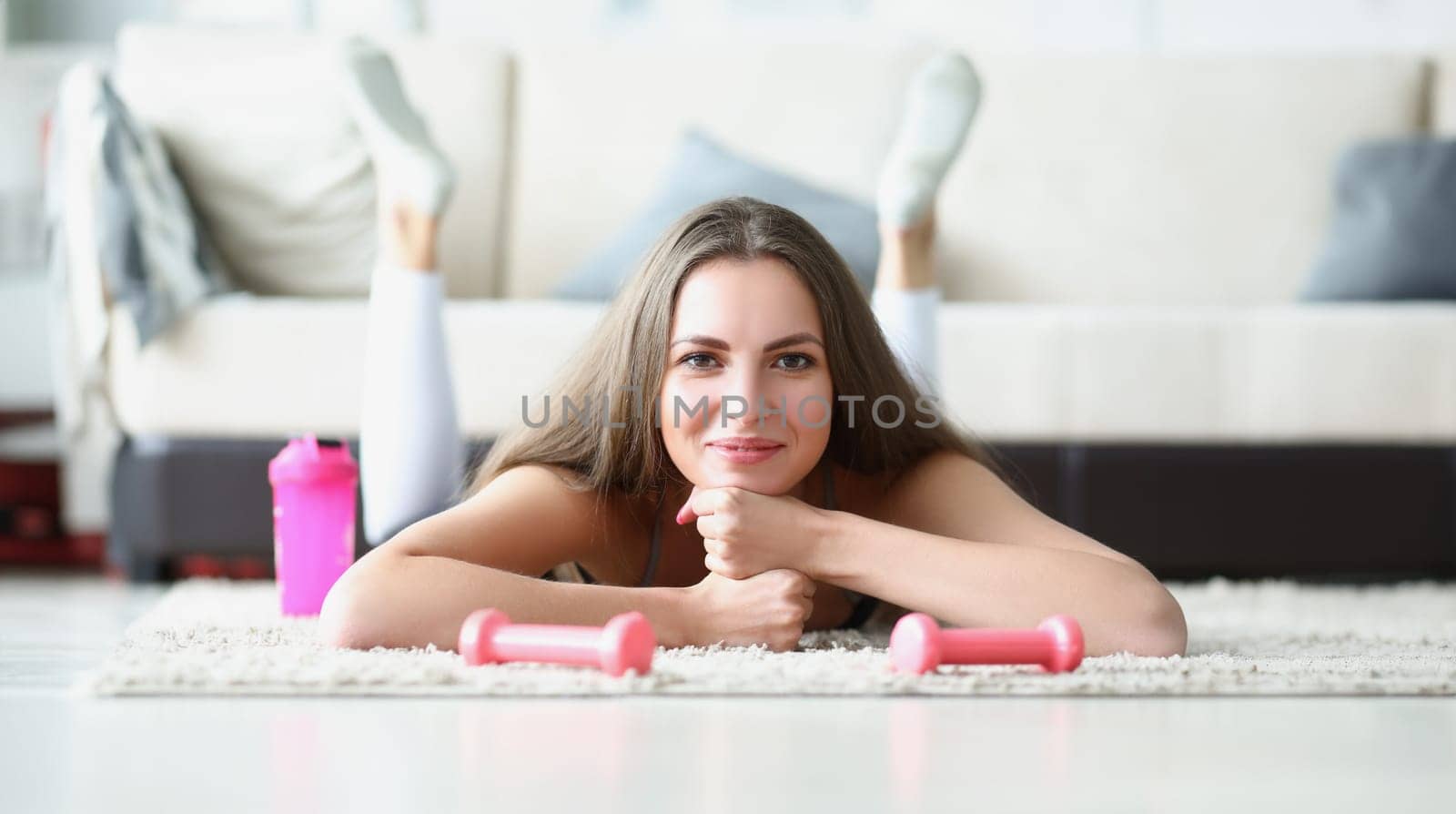 Young woman athlete with dumbbells in her hands lying on floor at home by kuprevich