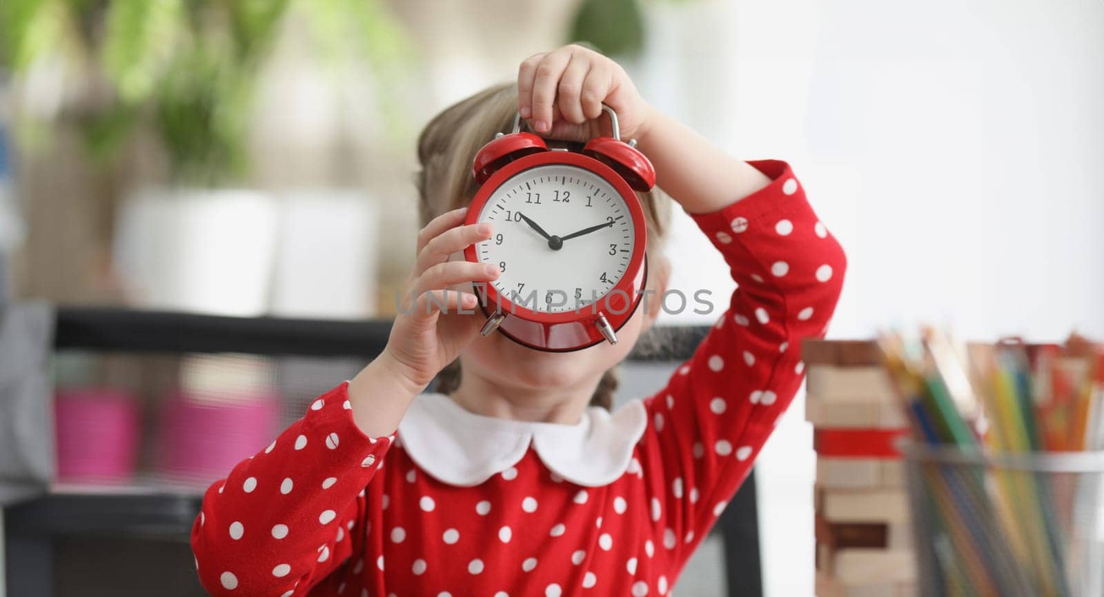 Little girl holding red alarm clock in front of her face. Sleep and wakefulness in children concept