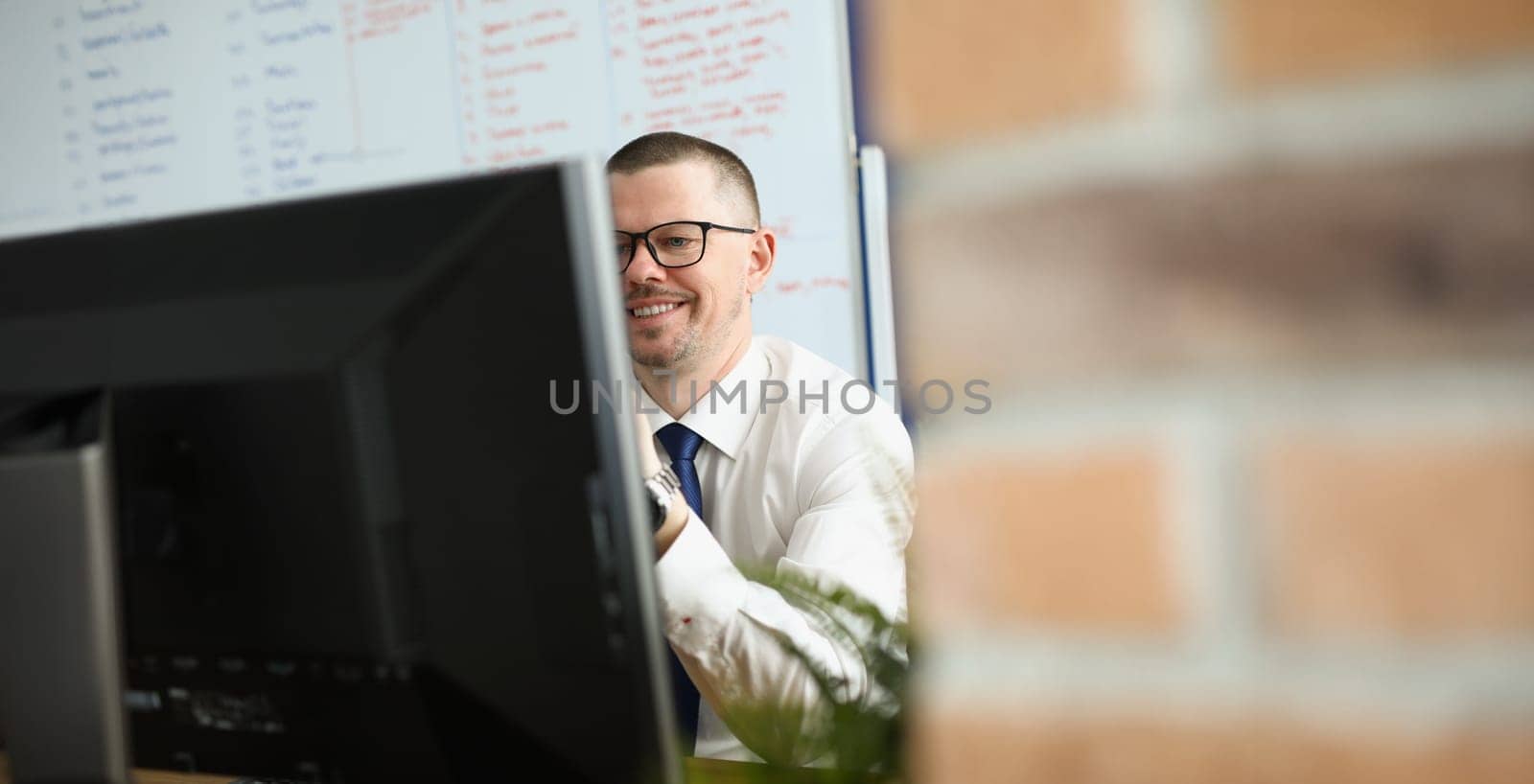 Businessman wearing glasses sitting at table in front of computer screen. Remote work concept