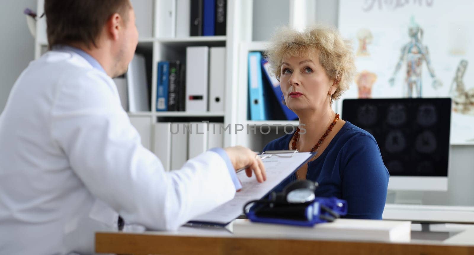 Doctor interviewing elderly woman patient in clinic office by kuprevich