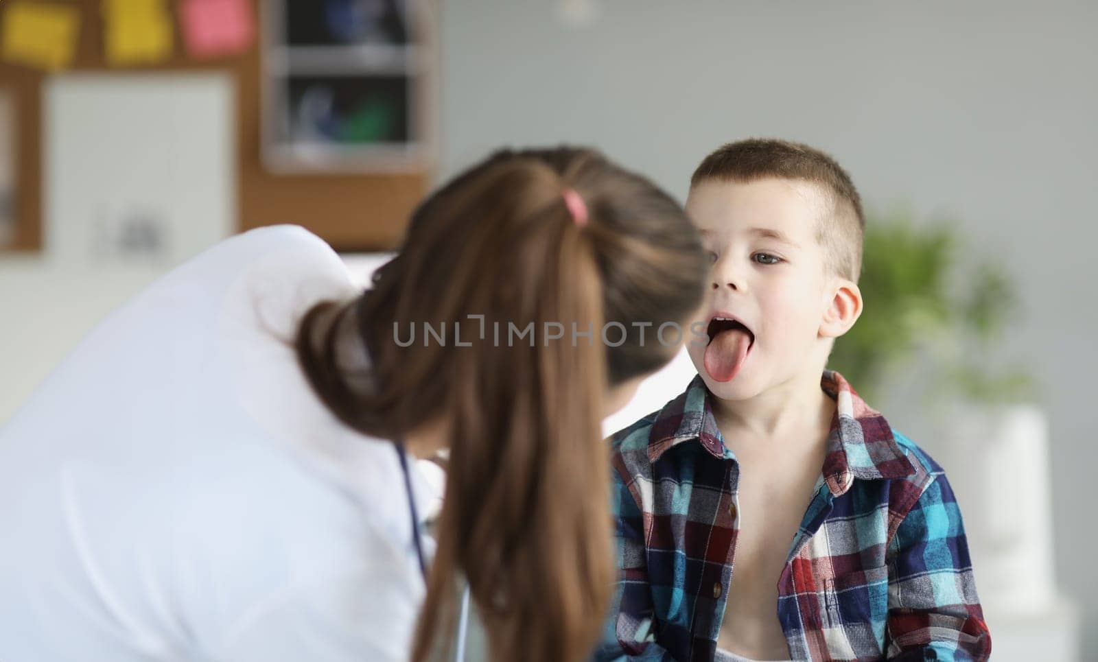 Doctor pediatrician examining throat of little boy in clinic. Treatment of seasonal colds in children concept