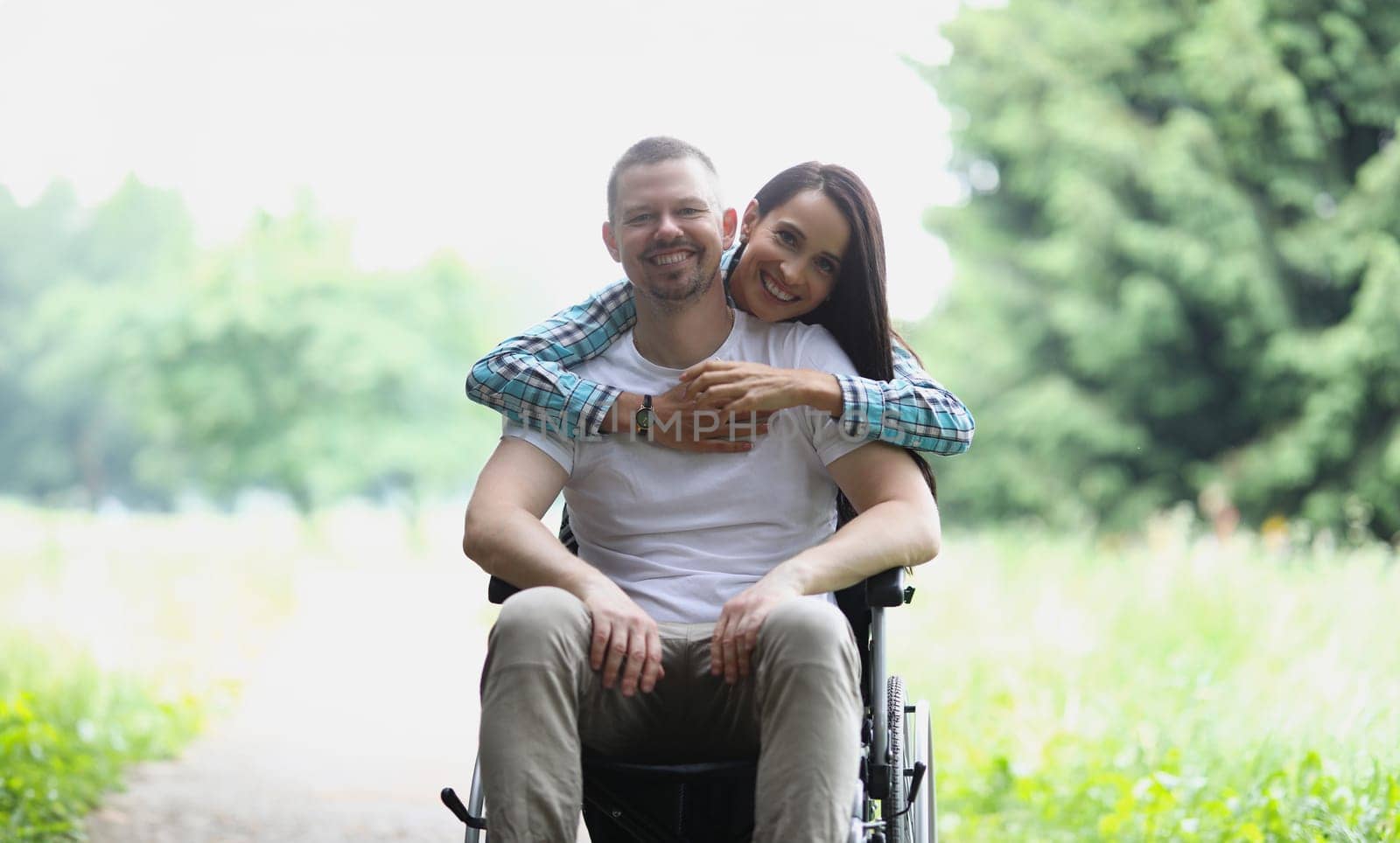 Woman hugging man in wheelchair in park portrait. Close relationship with disabled people concept