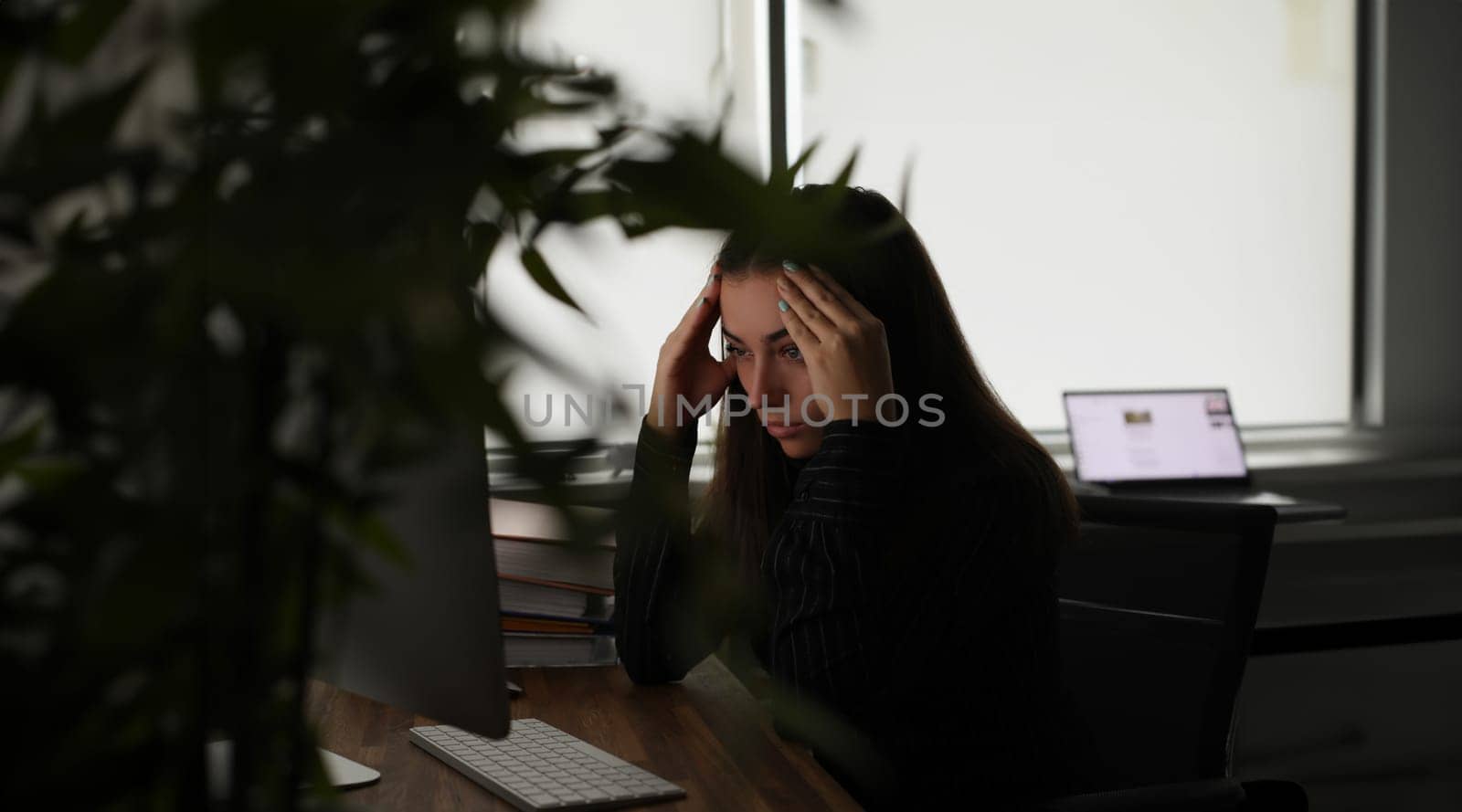 Tired woman holding her head with hands in front of computer screen in office. Headache when working at computer for long time concept
