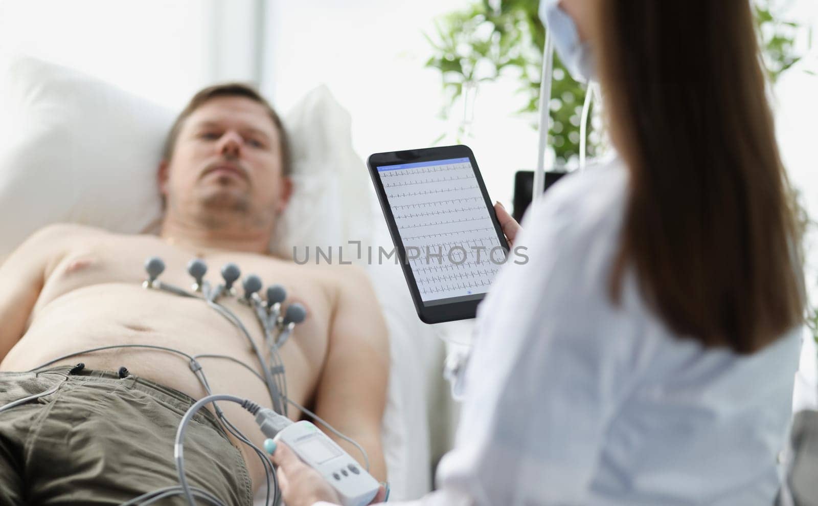 Doctor taking cardiogram to patient on couch in clinic closeup by kuprevich