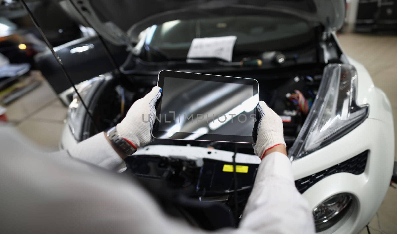 Master repairman holding digital tablet near open hood of car closeup. Modern car breakdown diagnostics concept