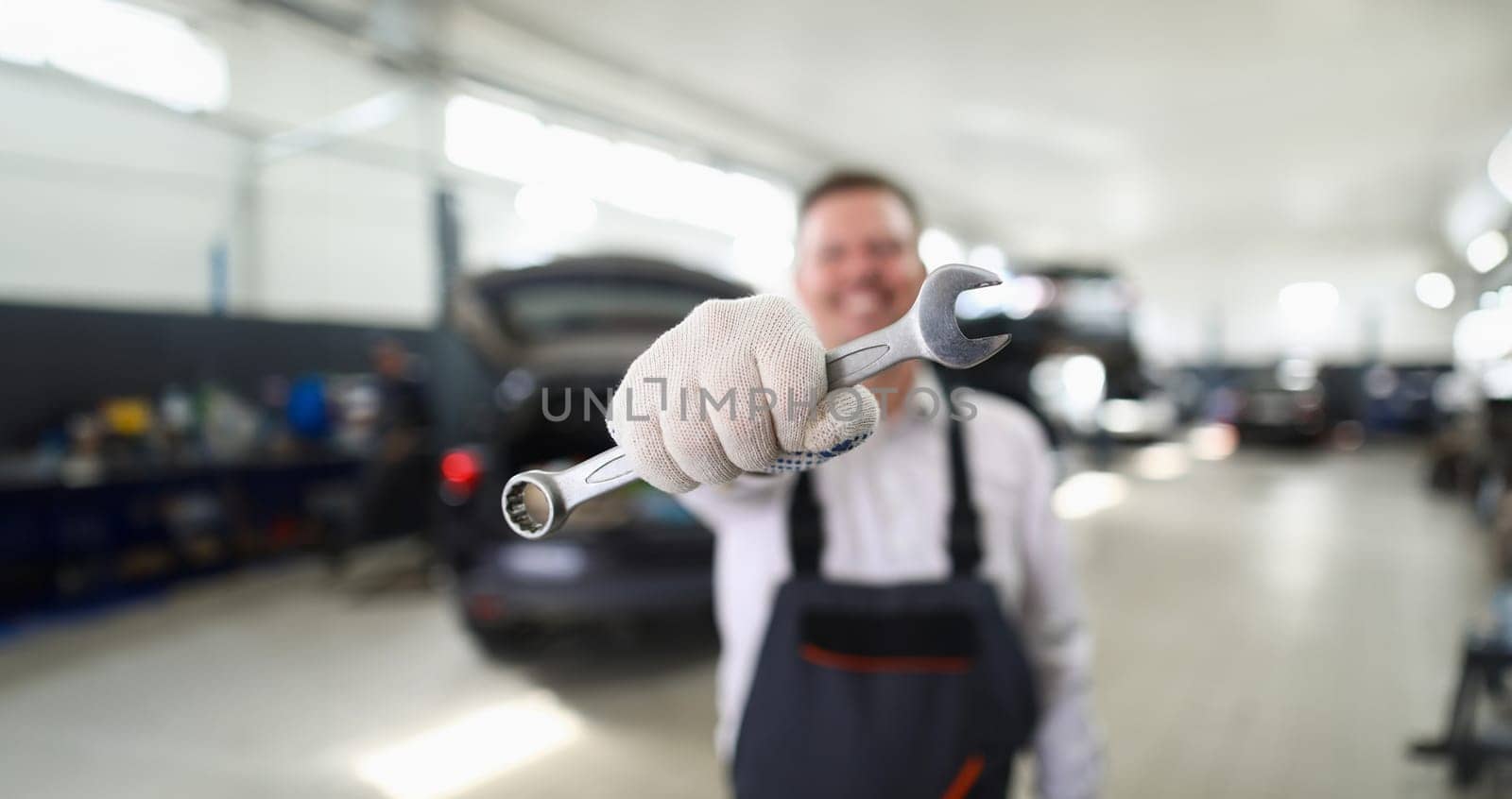 Male repairman holding wrench in car workshop closeup. Auto repair concept