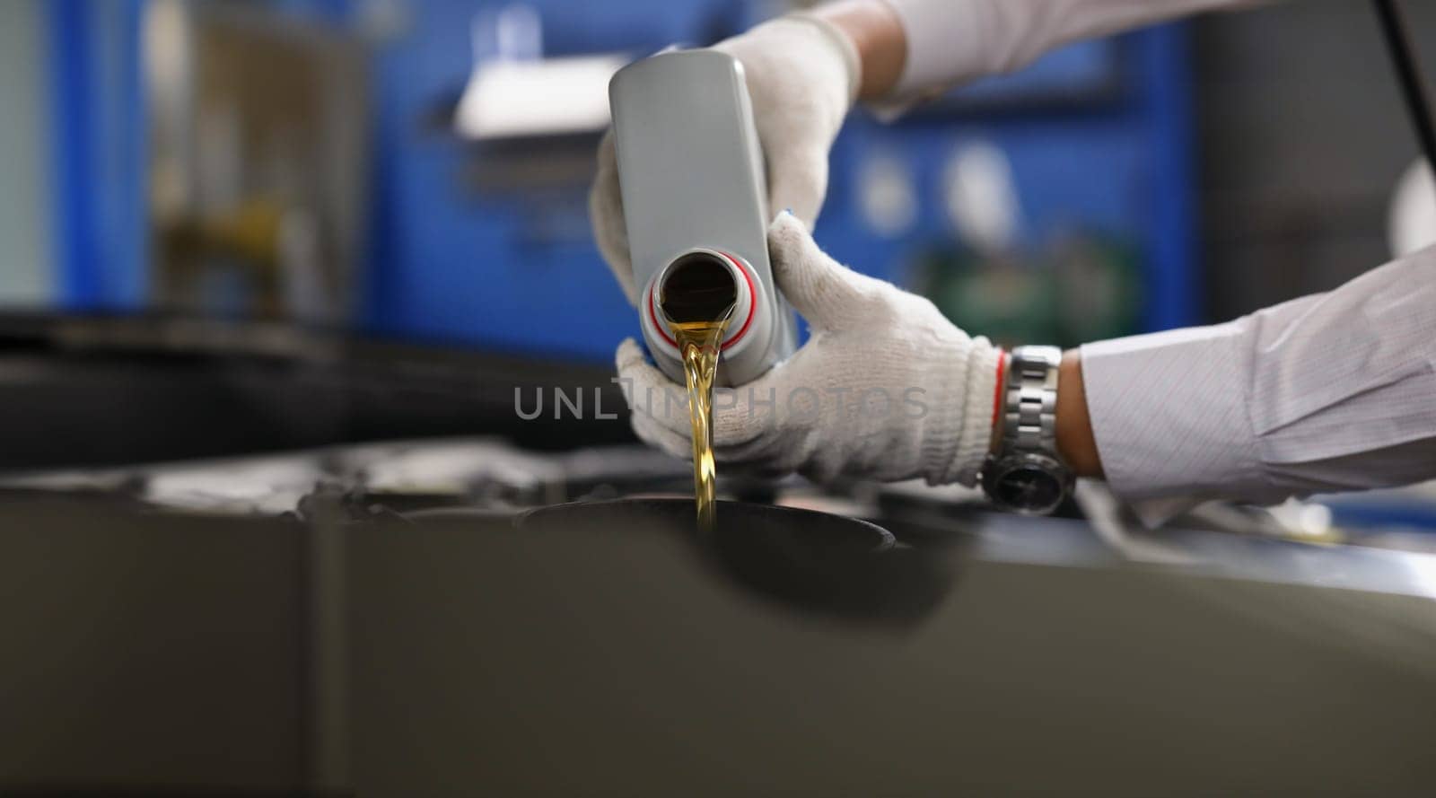 Master repairman pouring engine oil under hood of car closeup. Motor oil change interval concept