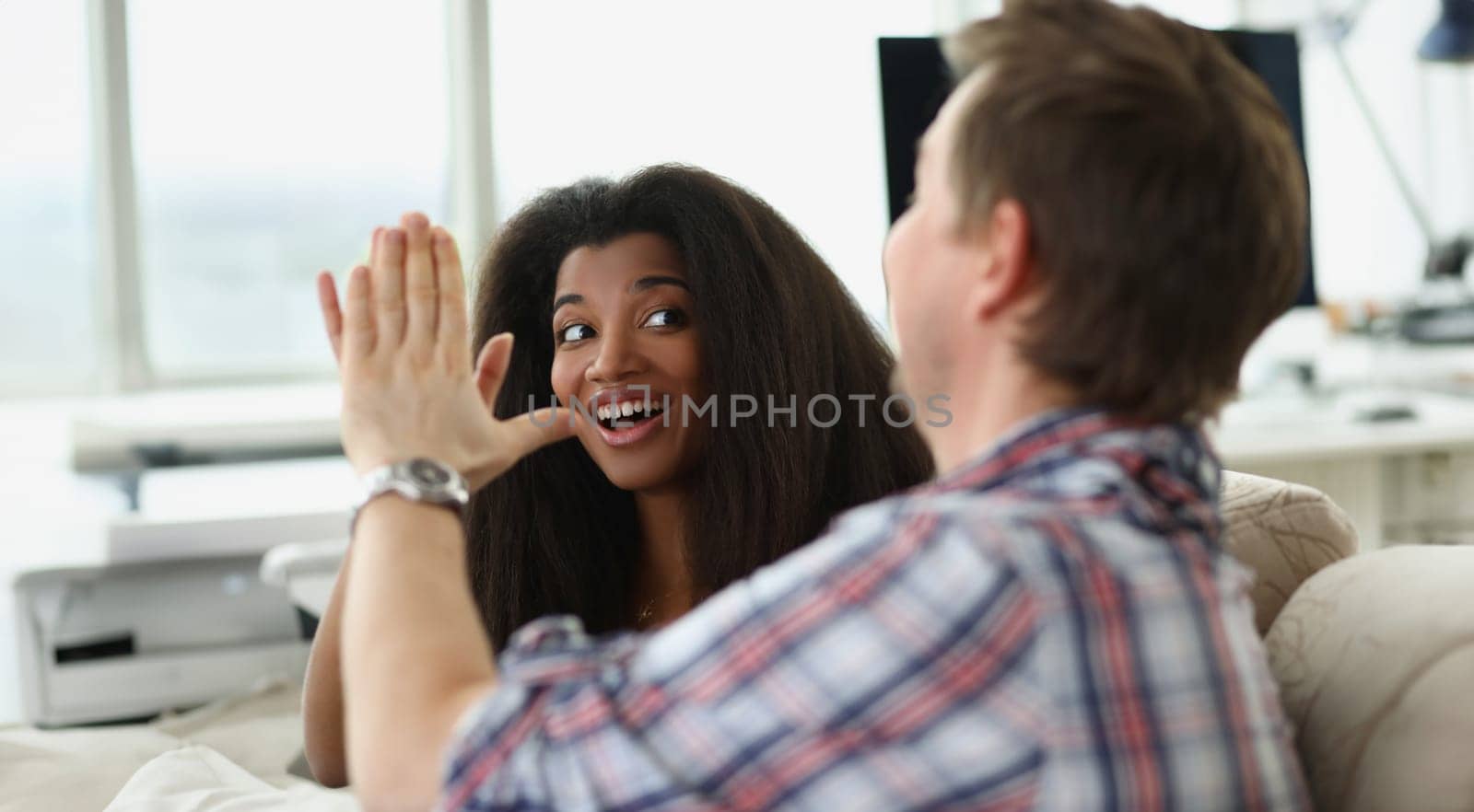 Caucasian man and african american woman sitting on sofa and giving high five. Friendship concept