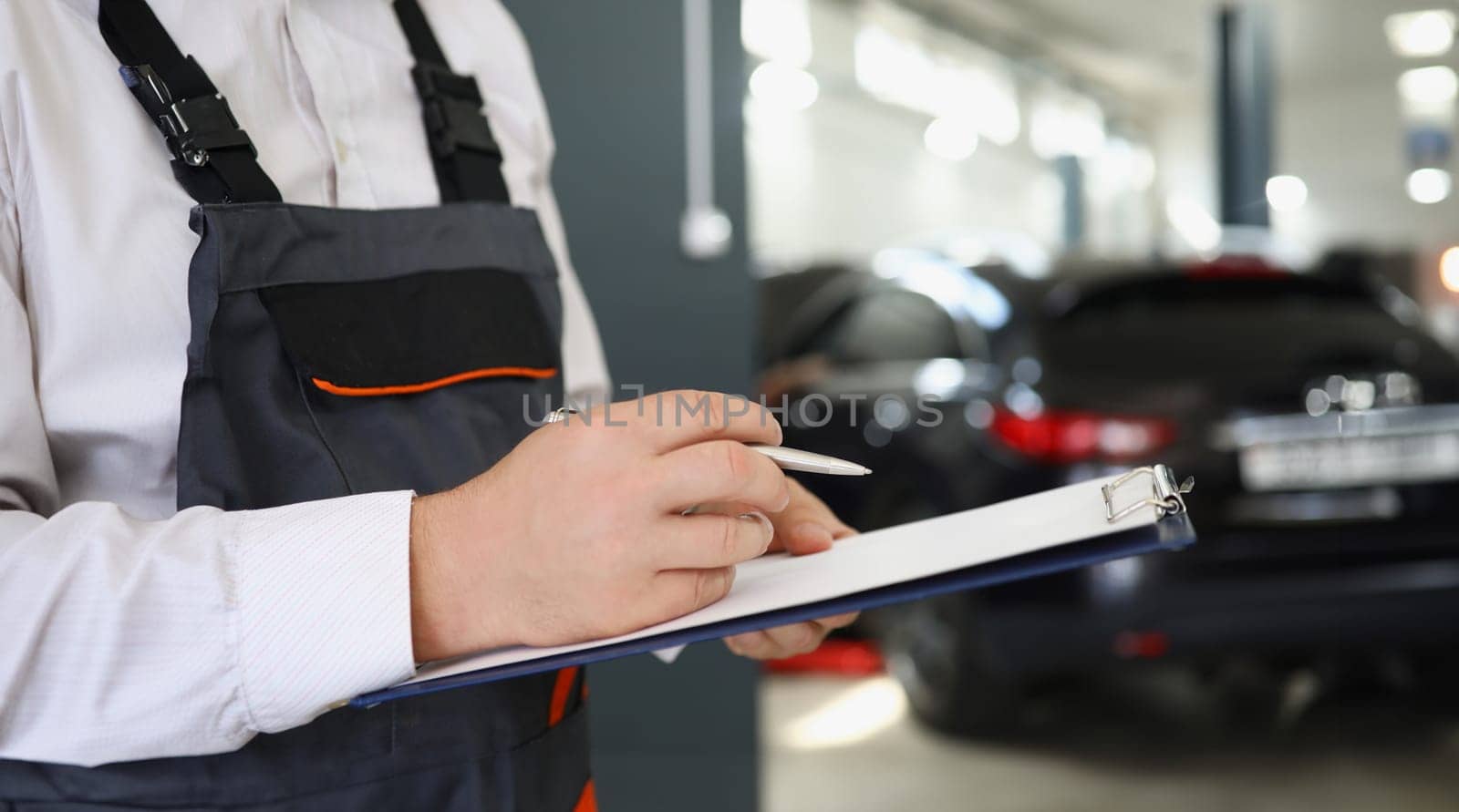 Man repairman standing with clipboard with documents at car repair shop closeup. Auto insurance concept