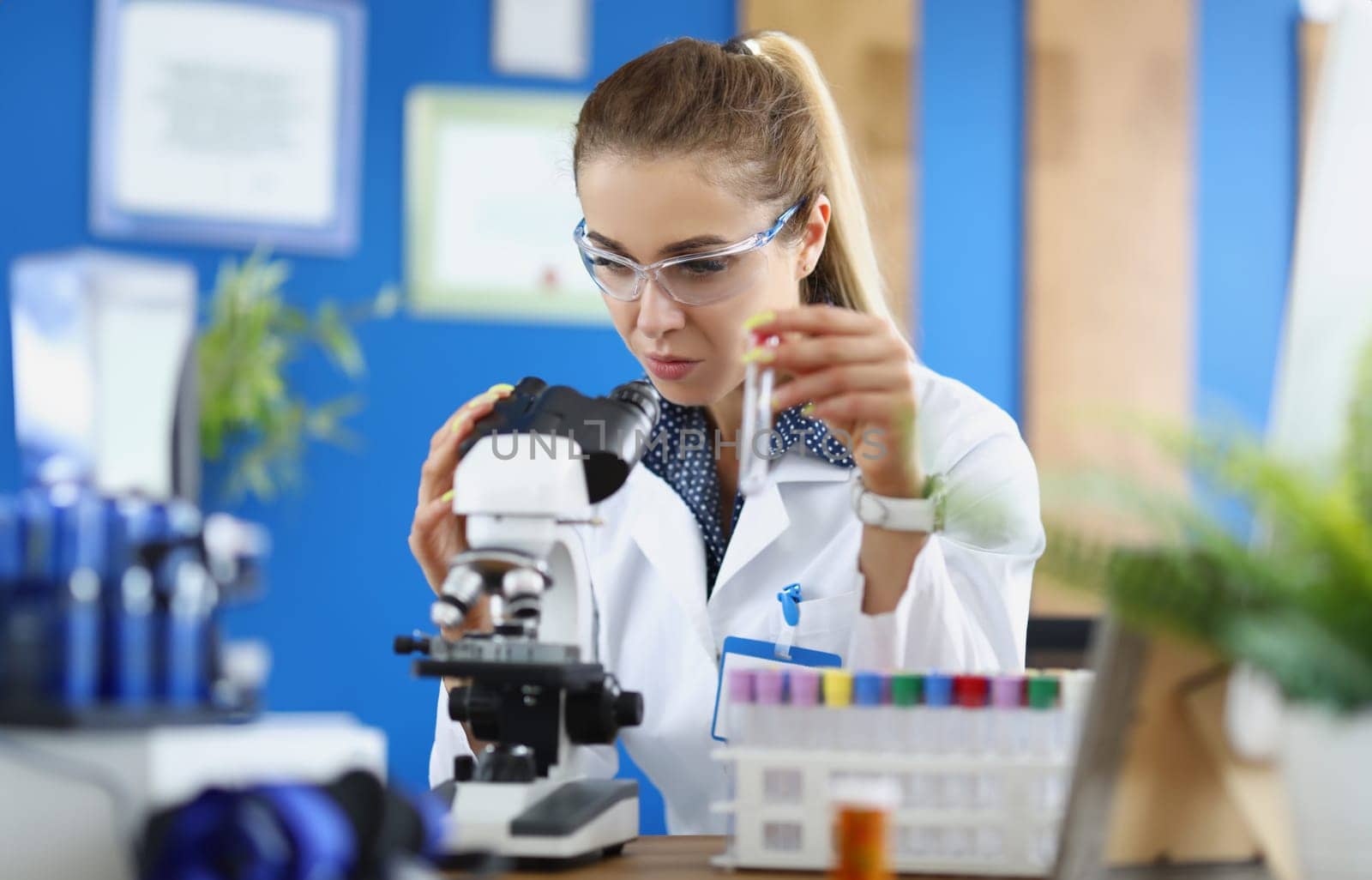 Woman scientist chemist looking through microscope and holding test tube. Laboratory diagnostics of internal diseases concept