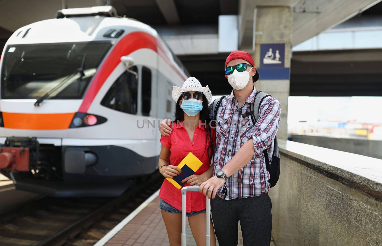 Young couple in protective medical masks standing near train with tickets in their hands by kuprevich