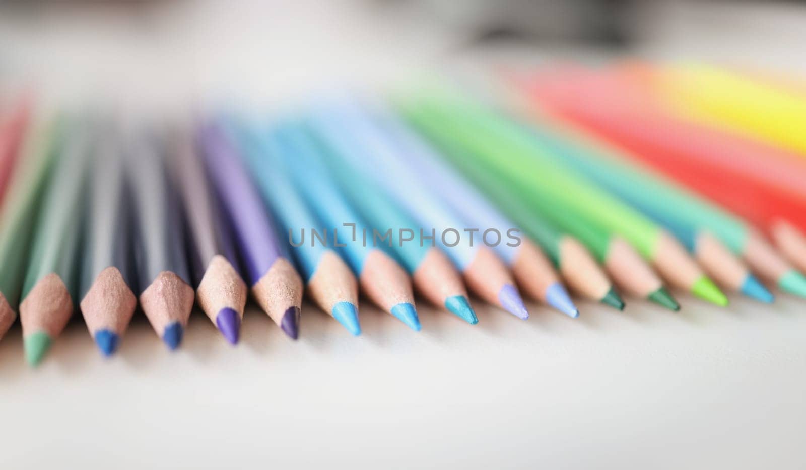 Many sharp multicolored pencils lying over colors of rainbow closeup background. School of fine arts concept