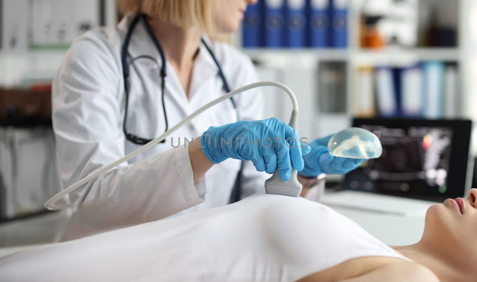 Doctor holding implant and doing ultrasound examination of woman breasts closeup. Annual preventive ultrasound examinations after mammoplasty concept