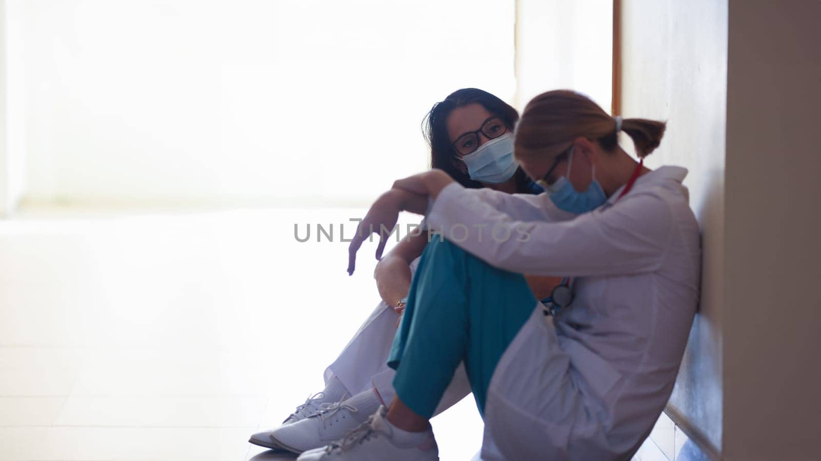 Tired women doctors wearing protective medical masks sitting in clinic corridor by kuprevich