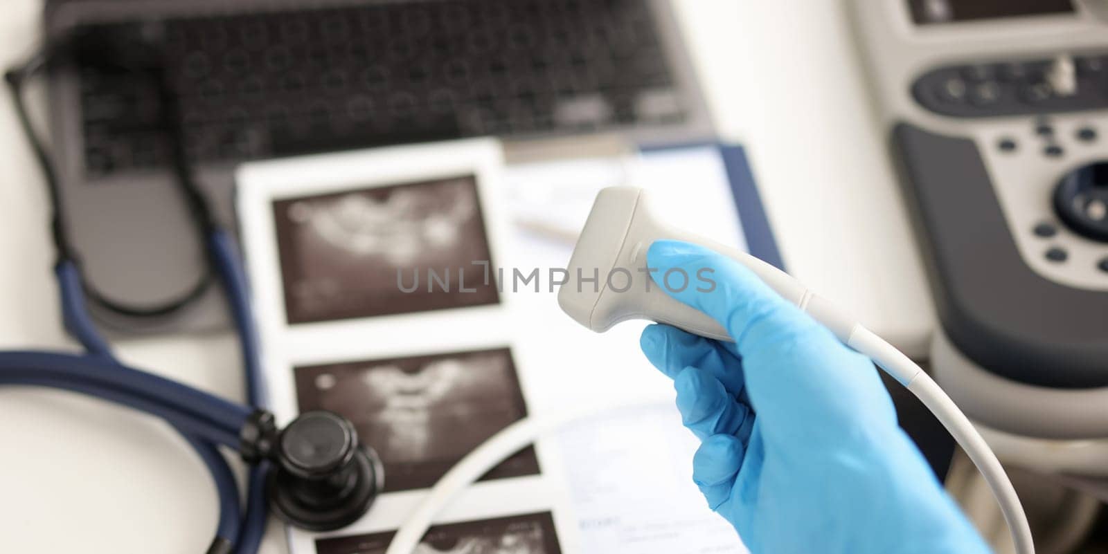 Doctor holding ultrasound probe against background of pictures and medical documents closeup. Instrumental diagnostics in medicine concept