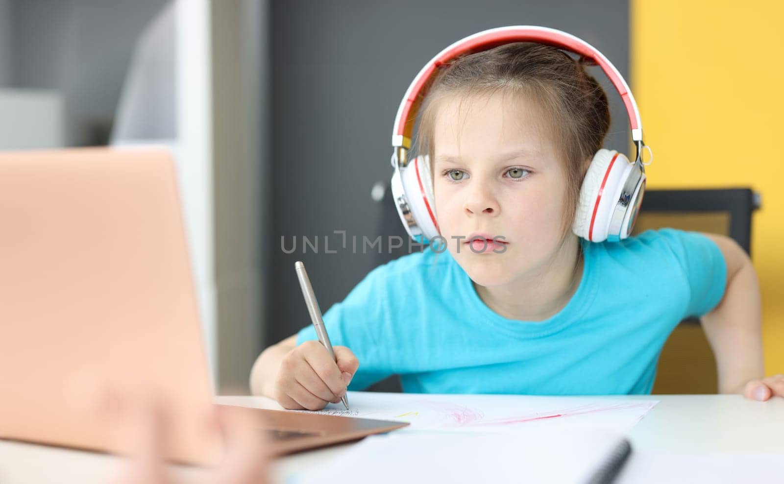 Little girl schoolgirl in headphones sitting in front of laptop at home by kuprevich