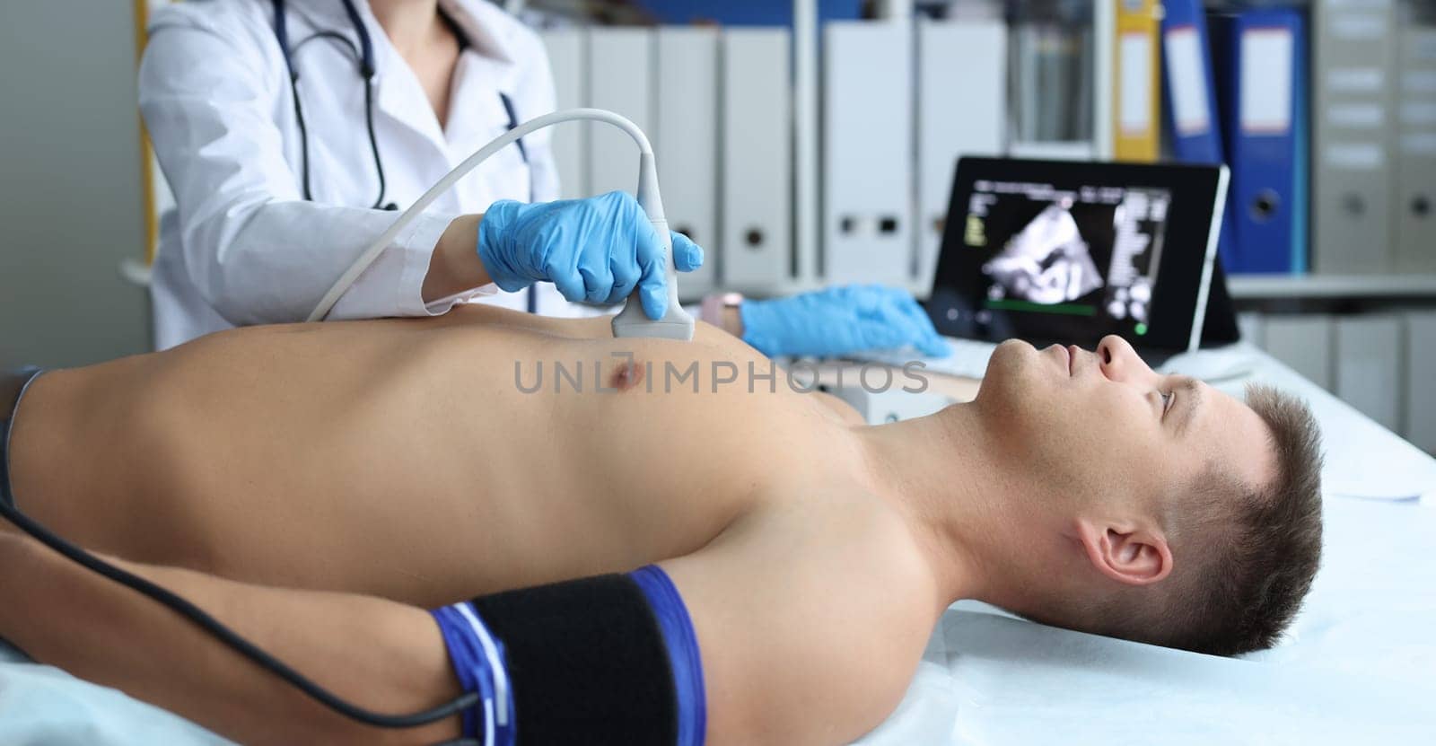 Doctor doing heart ultrasound to young male patient in clinic by kuprevich