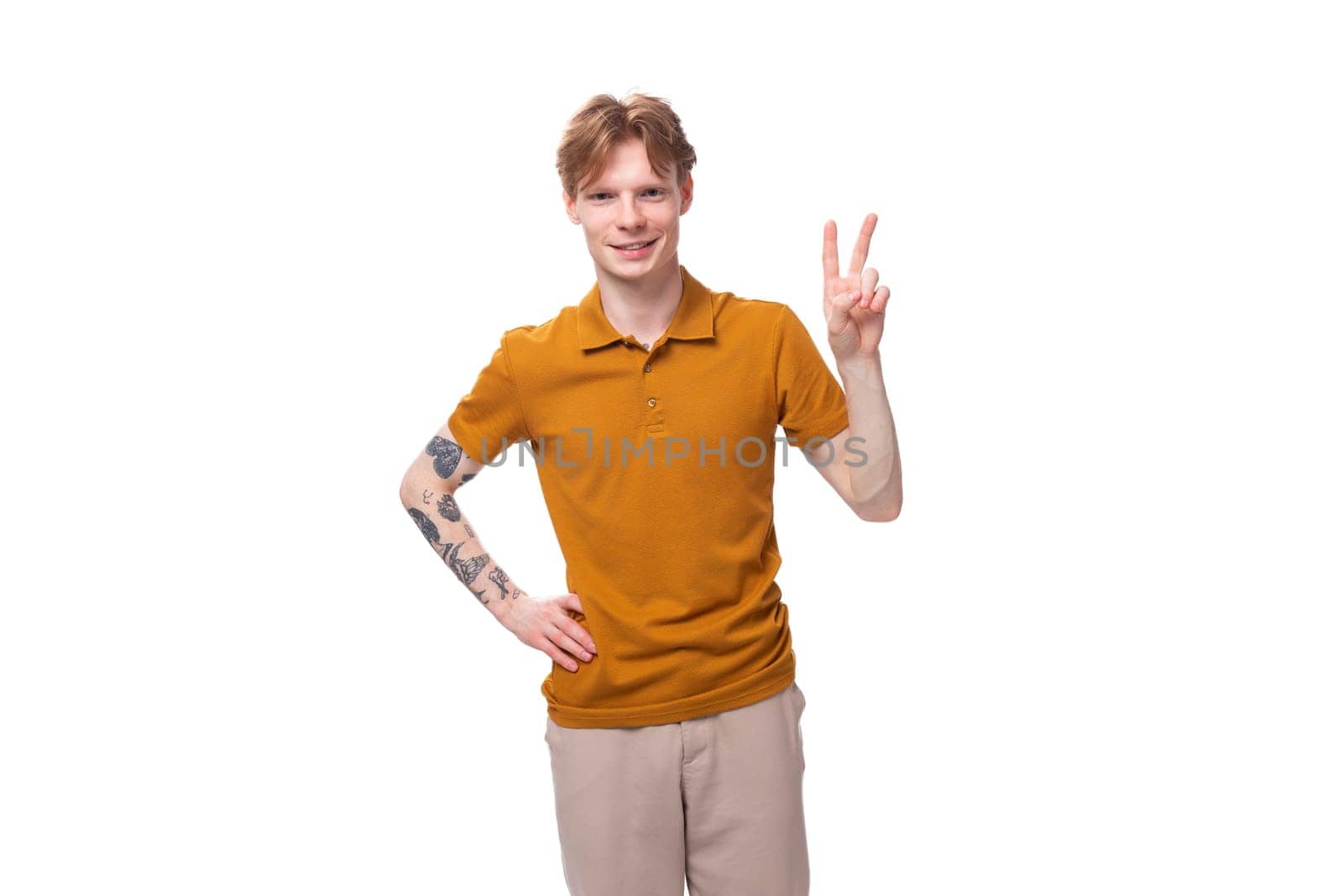 young red-haired caucasian student man with a tattoo dressed in a mustard t-shirt gesturing by TRMK