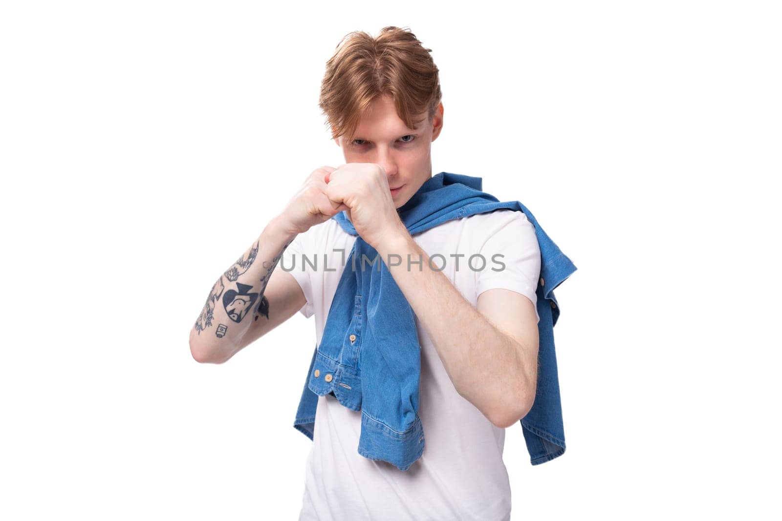 young fashionable caucasian guy with short red hair with a tattoo on his arms is dressed in a white t-shirt on a white background with copy space.