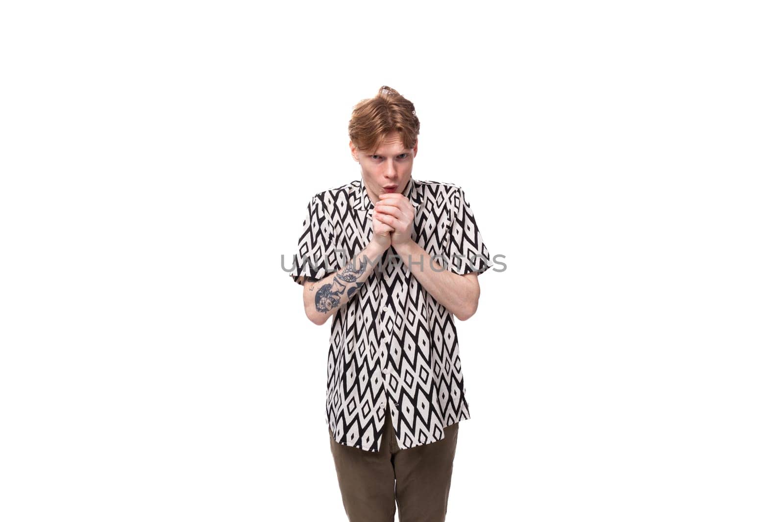 a young caucasian man with red hair with a tattoo dressed in a summer black and white shirt is waiting and thinking against the background with copy space.