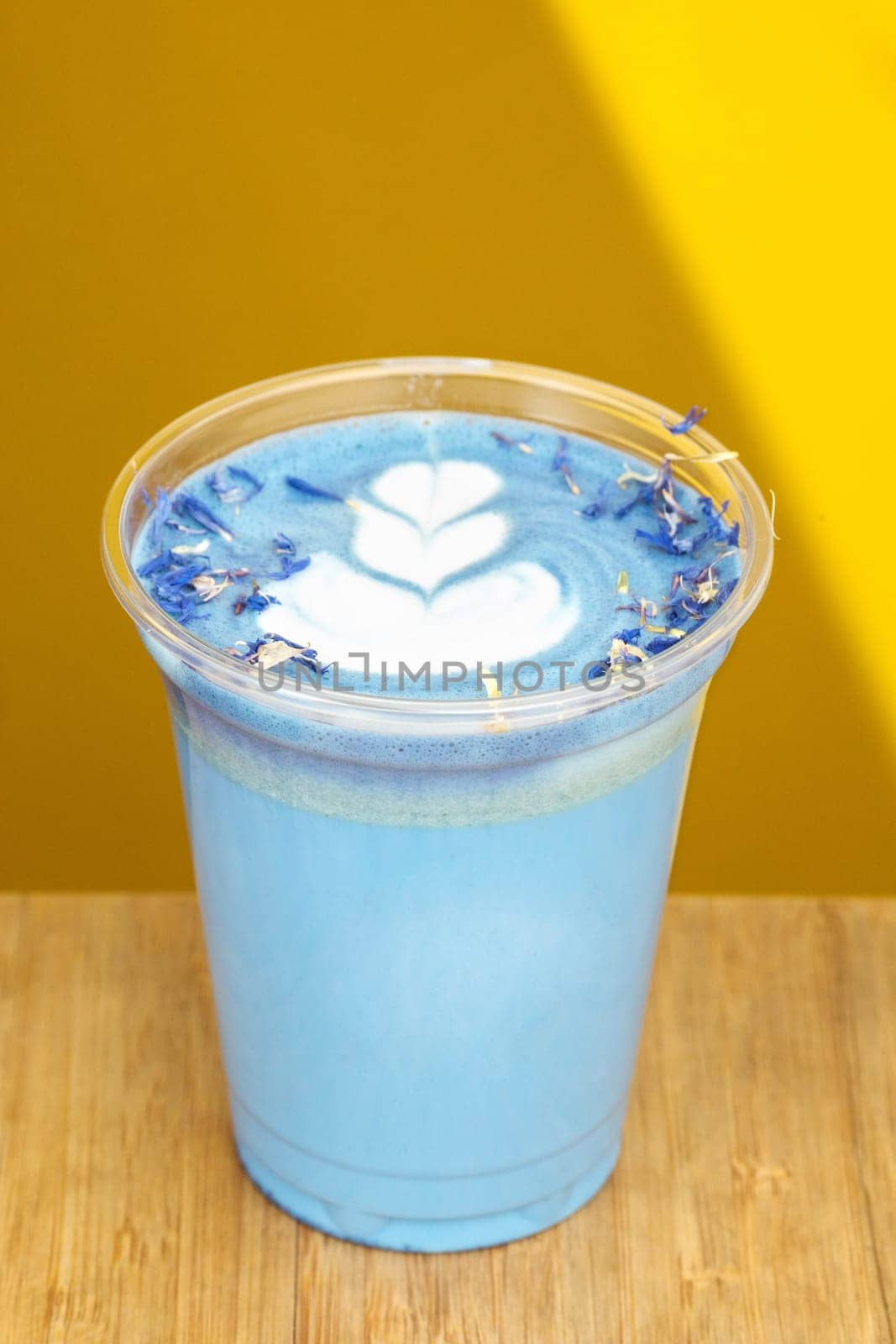Hot fresh milk with butterfly pea latte art along with added flavor in glass and placed on wooden table in room with yellow wall in daylight