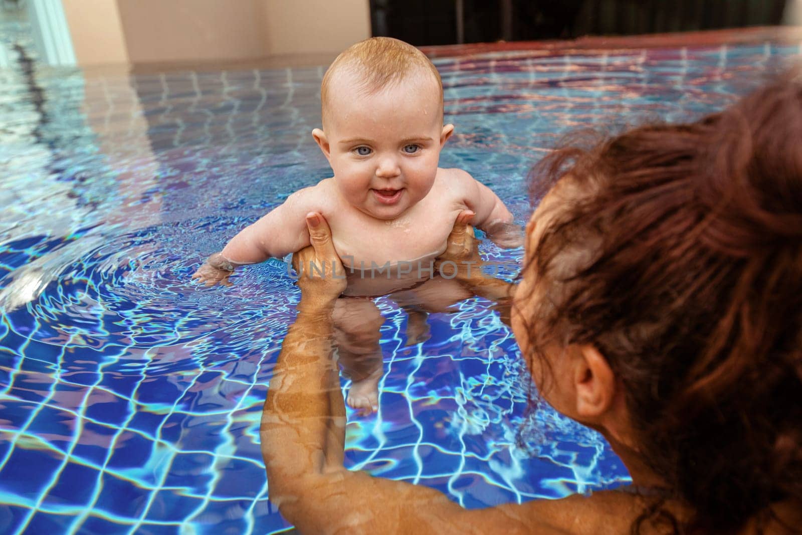 Crop shot from above parent carrying little infant kid in water of pool learning to swim