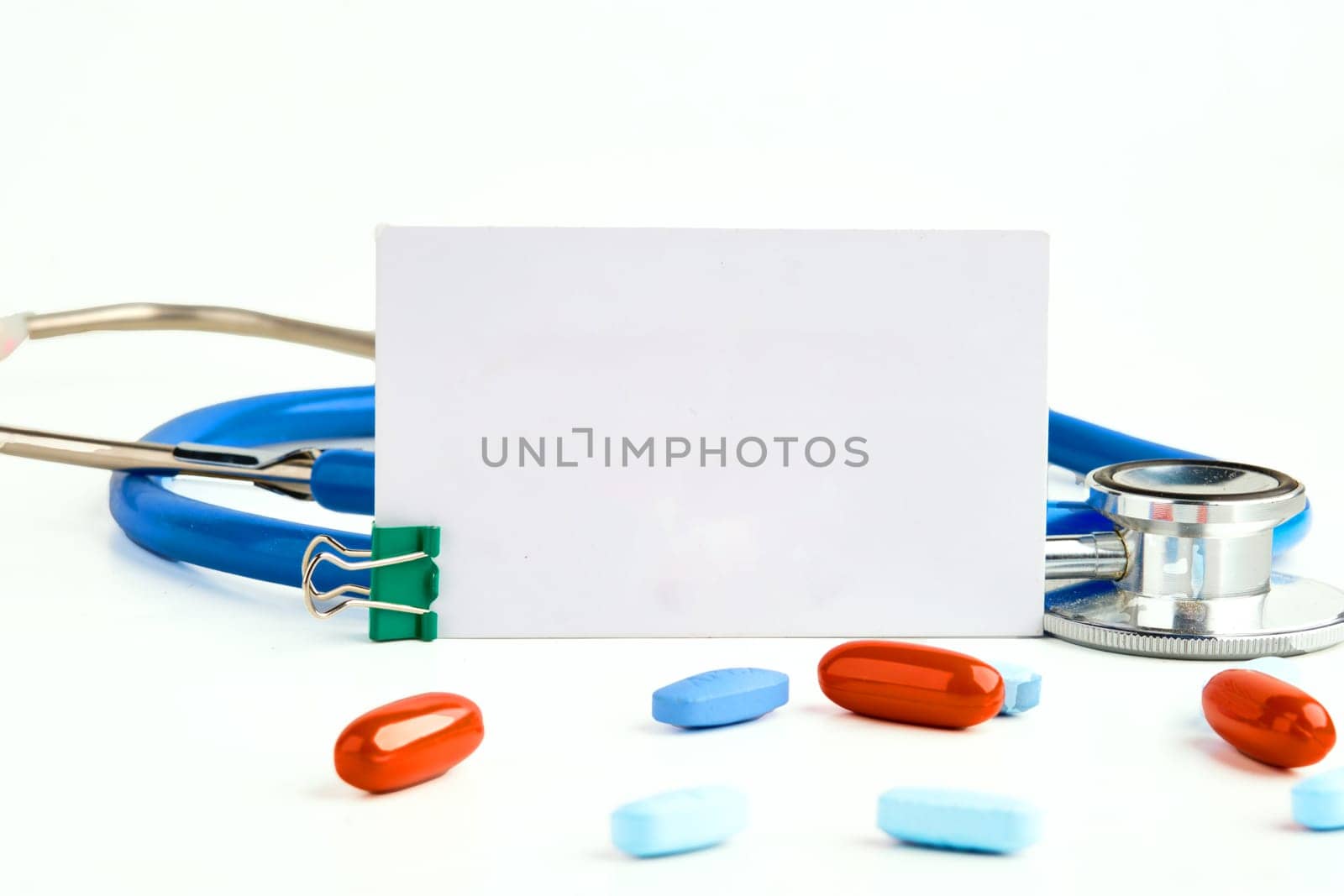 A white card, a stethoscope and pills on a white background. Copy space