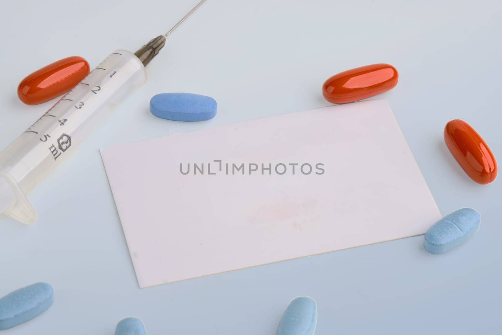 A card, pills, a syringe on a light background. Copy space