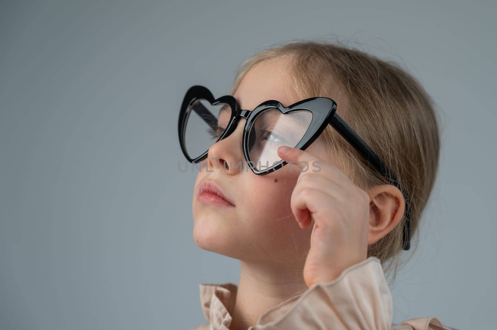 Portrait of a cute little girl wearing heart-shaped glasses on a white background