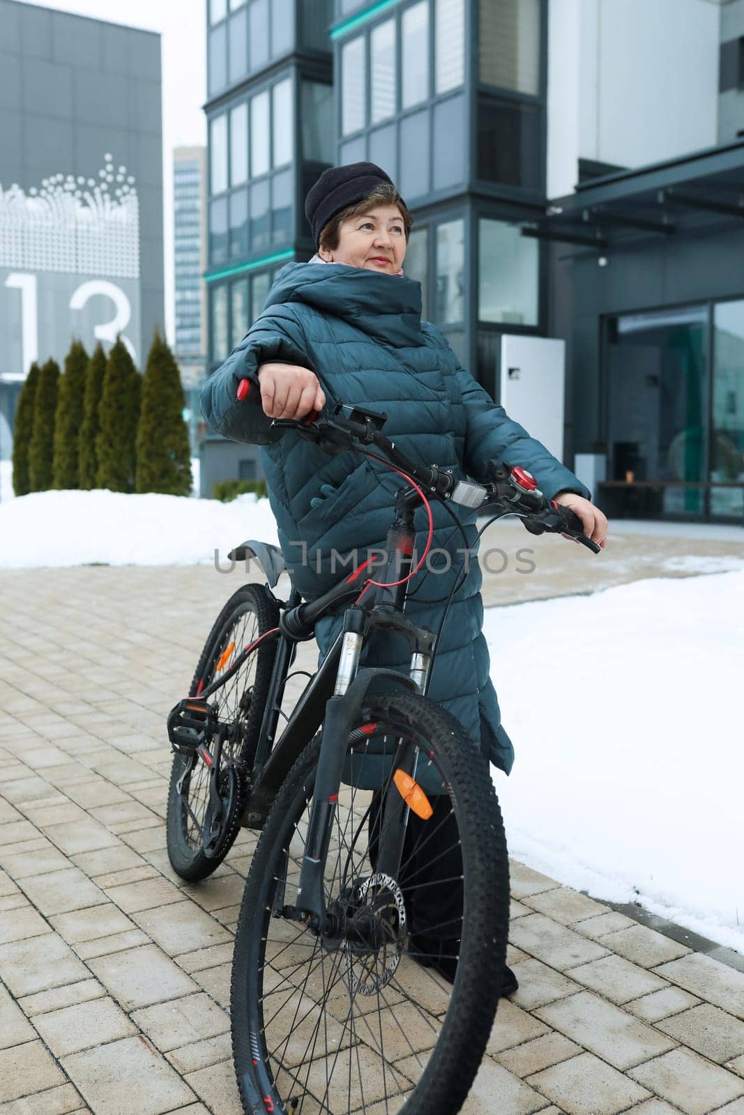 Mature European woman dressed in a winter coat rides a bicycle along the city streets.