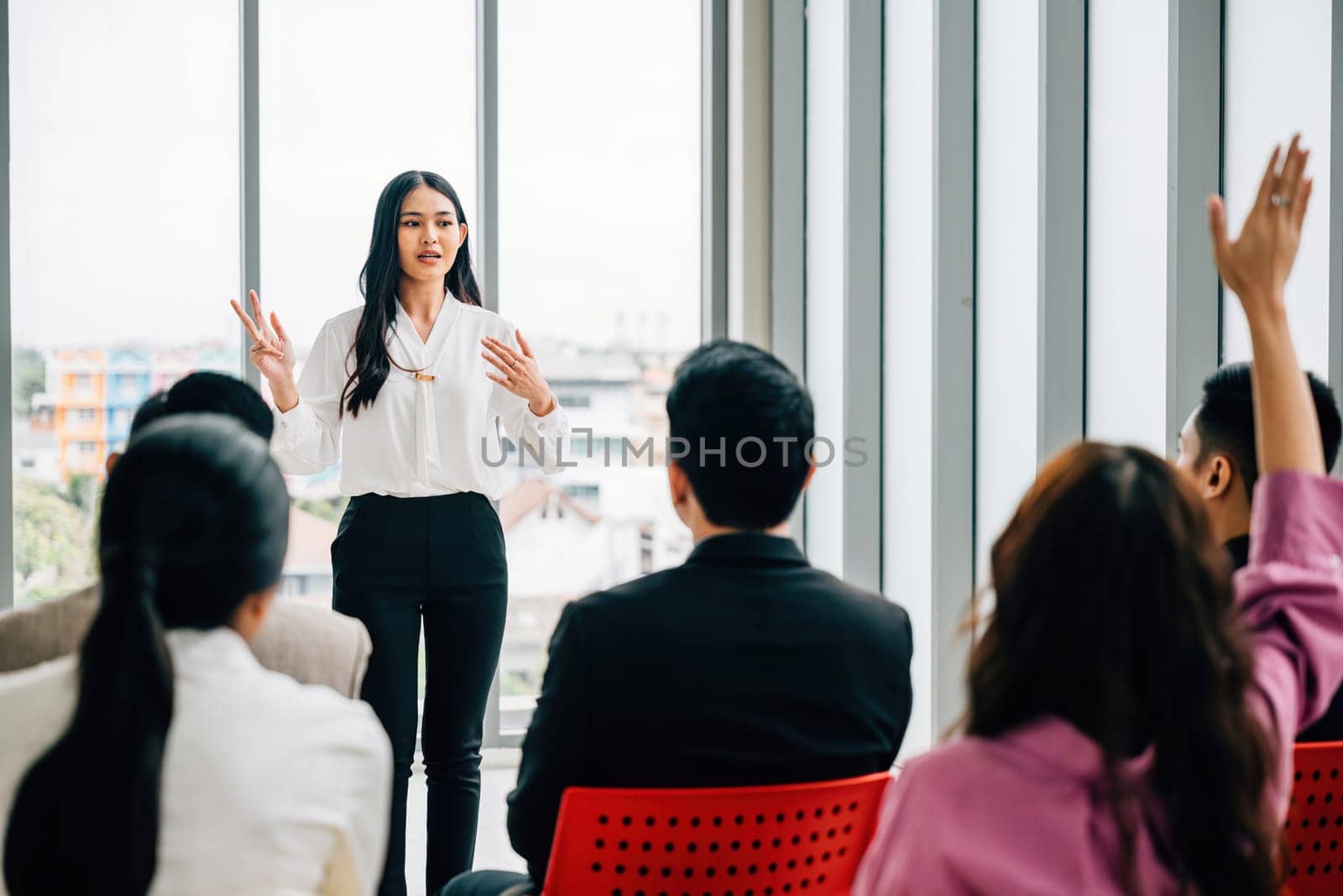 In a seminar classroom, a large group raises their hands to actively engage in the discussion. This audience is brimming with answers in a dynamic conference atmosphere.