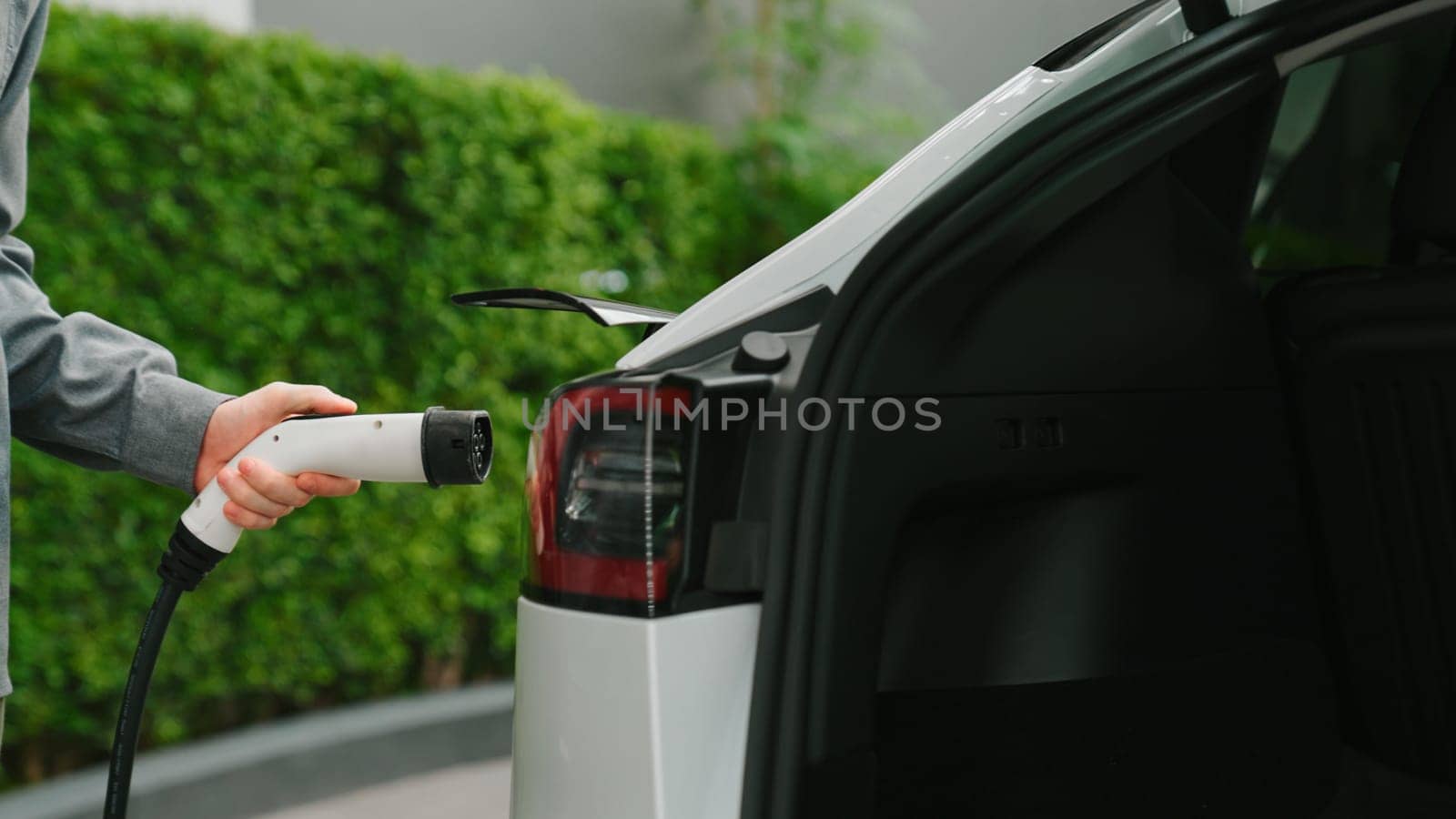 Young man recharge EV electric car in green sustainable city outdoor summer garden as lifestyle of young people in urban sustainability green clean rechargeable energy of electric vehicle innards