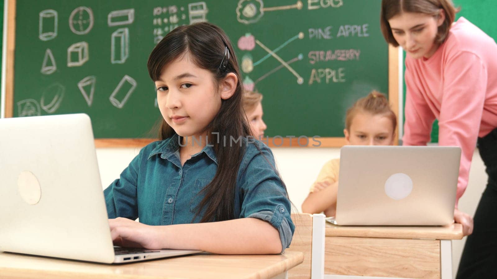 Smart asian girl looking at camera while coding engineering prompt. Multicultural student learning about generated AI while teacher teaching about system or checking classwork at STEM class. Pedagogy.
