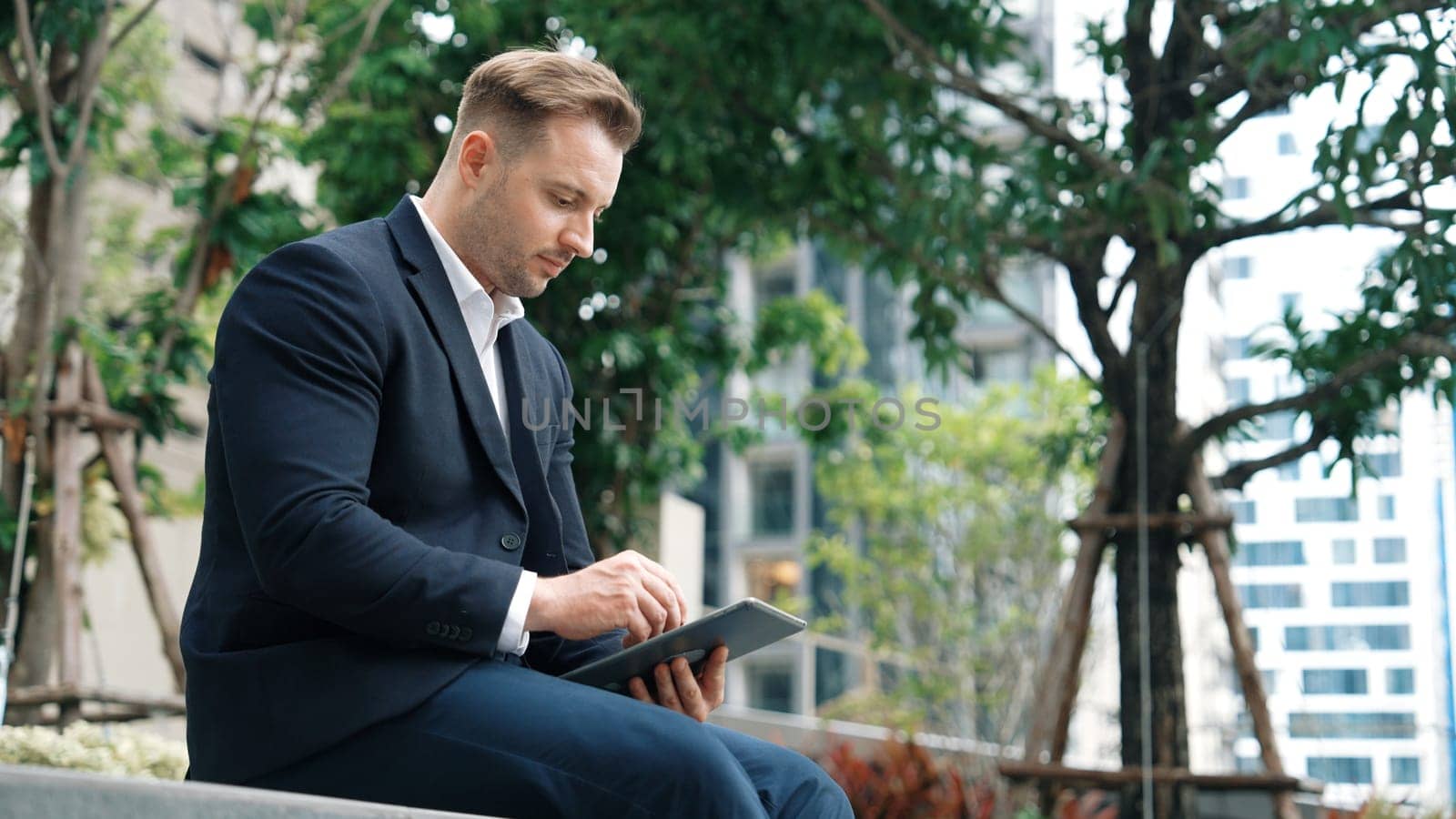 Businessman sitting at park while working on tablet by reading report. Urbane by biancoblue