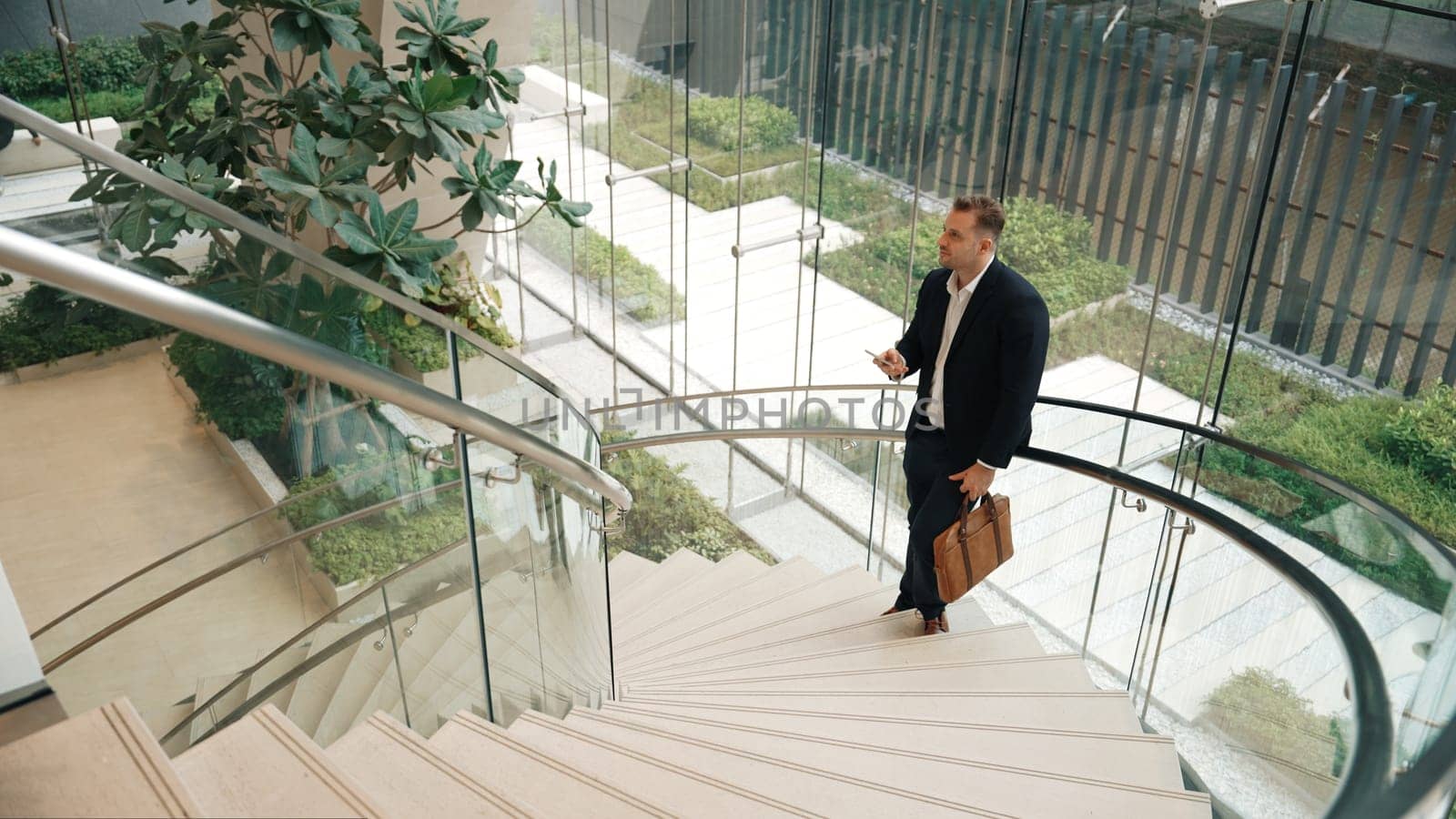 Caucasian businessman analyzing marketing data from mobile phone and making decision at modern glass wall building. Happy project manager checking start up project sales report while standing. Urbane