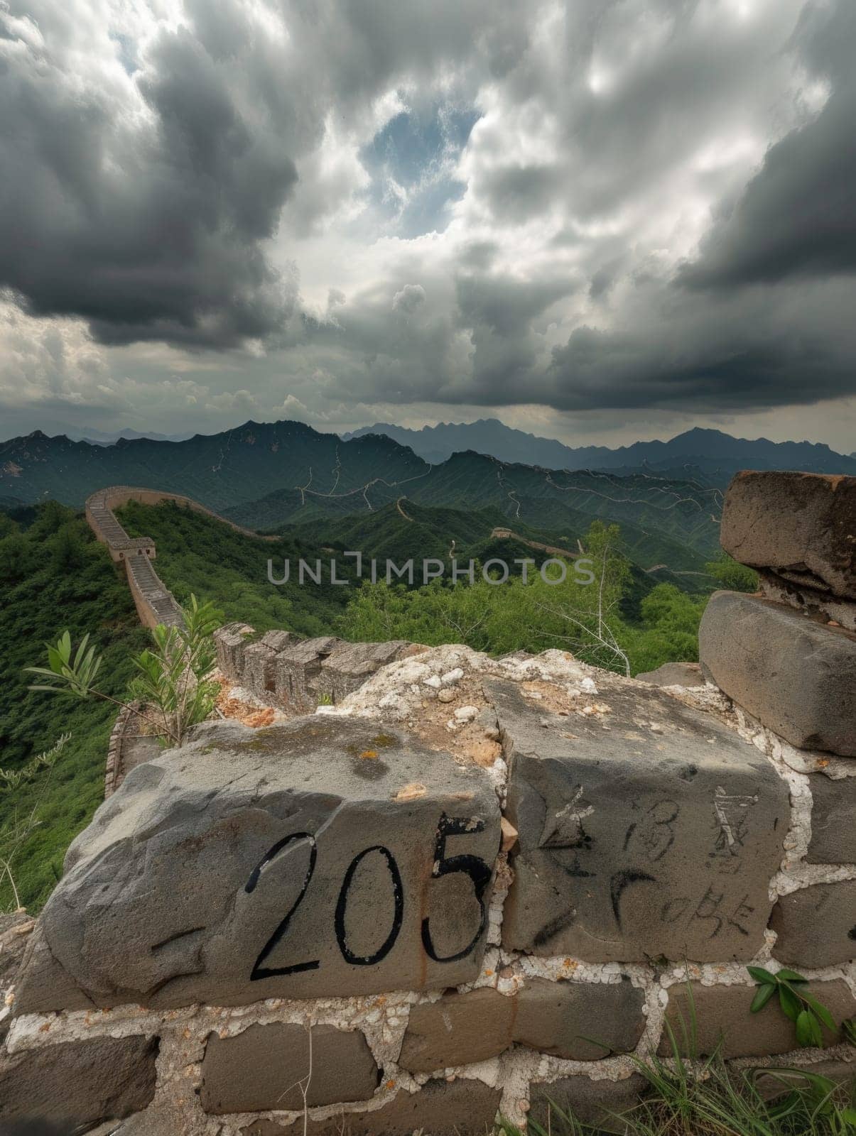 A photograph showing a stone wall with writing on it, set against a backdrop of cloudy skies.