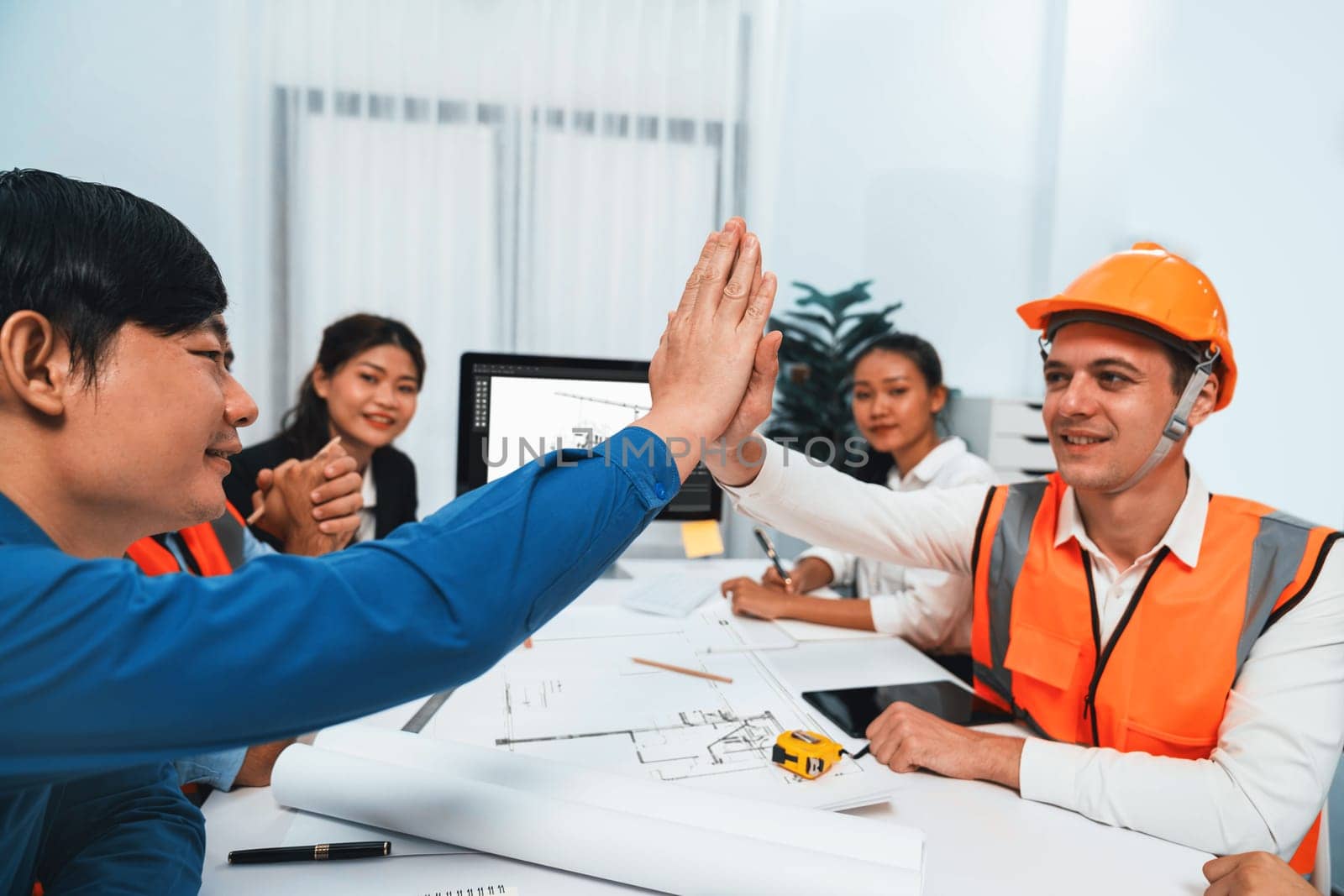 Diverse group of civil engineer and client celebrate and high five after make successful agreement on architectural project, reviewing construction plan and building blueprint at meeting table.Prudent