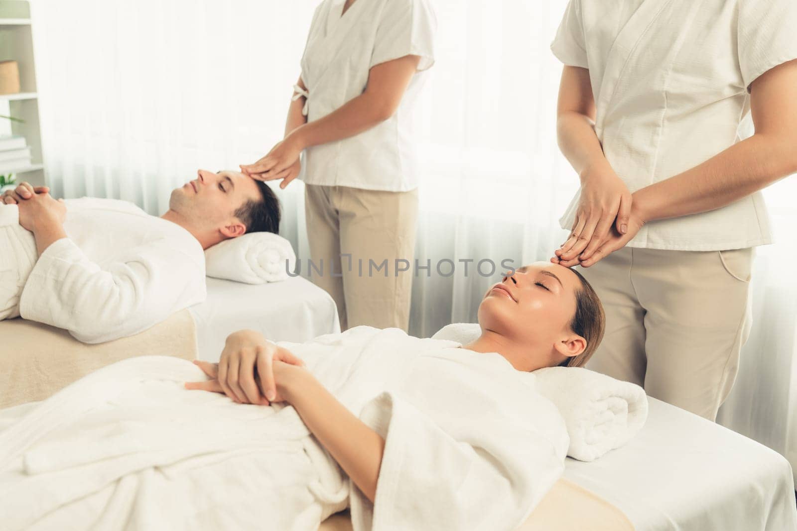 Caucasian couple enjoying relaxing anti-stress head massage and pampering facial beauty skin recreation leisure in dayspa modern light ambient at luxury resort or hotel spa salon. Quiescent