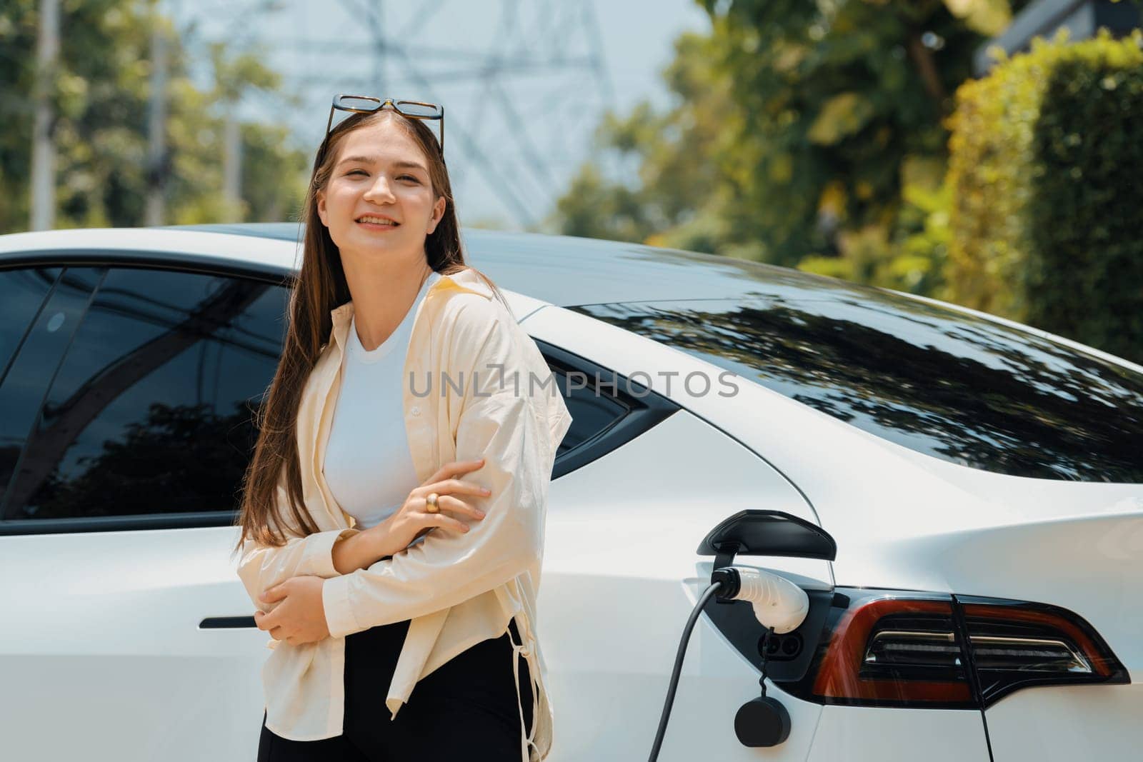 Young woman recharge her EV electric vehicle at green city park parking lot. Urban sustainability lifestyle for environmental friendly EV car with battery charging station. Expedient